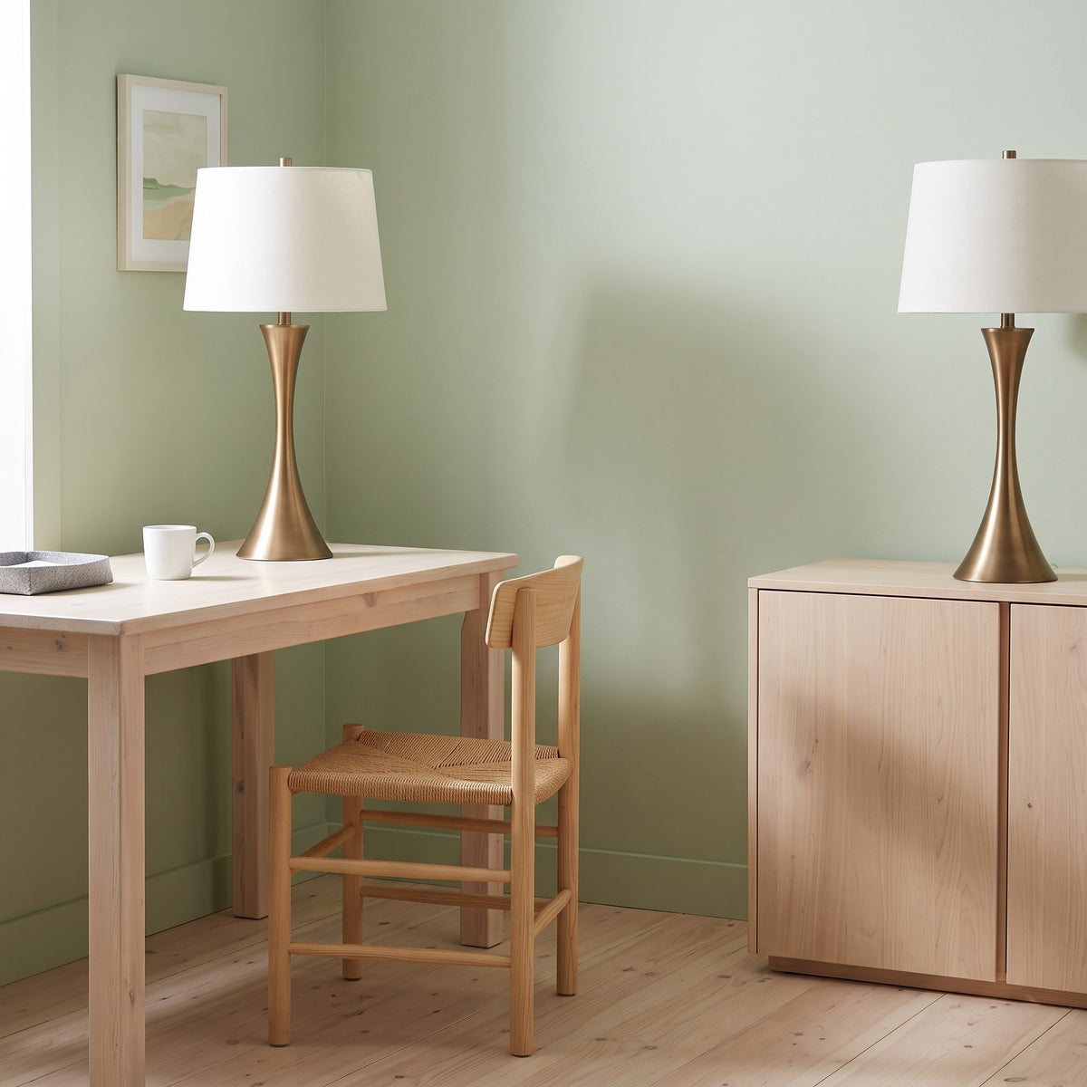 Pair of brass finish table lamps with off-white linen drum shades on a wood desk and cabinet against a sage green wall