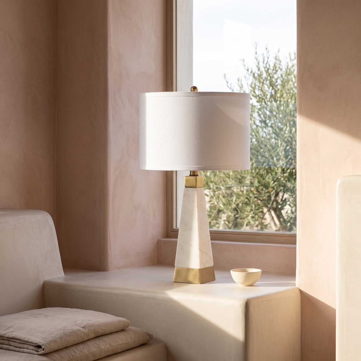 White marble table lamp with gold finish base and white fabric drum shade on a plaster window ledge