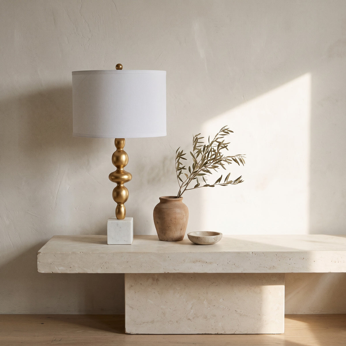 Gold finish table lamp with white marble cube base and white drum shade on a low stone bench