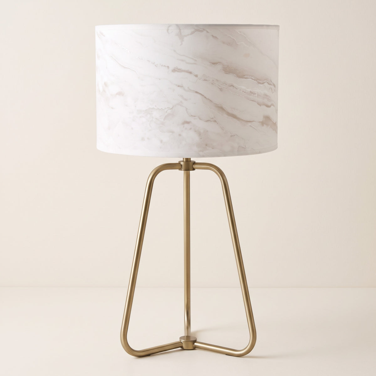 White marble-look drum shade table lamp with brass finish tripod base on an ivory backdrop