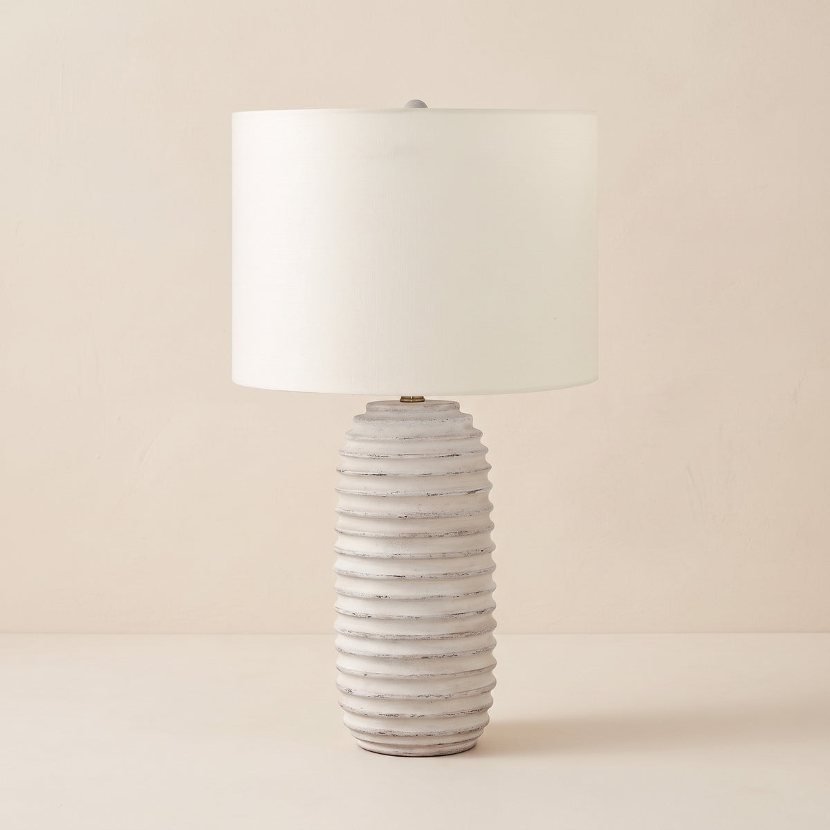 Cream ribbed resin table lamp with ivory linen-look drum shade on a warm ivory plaster backdrop