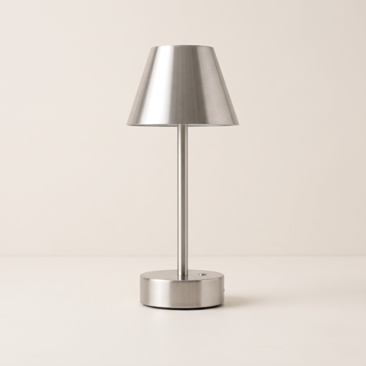 Brushed nickel cordless table lamp with tapered metal shade and round base on an ivory backdrop
