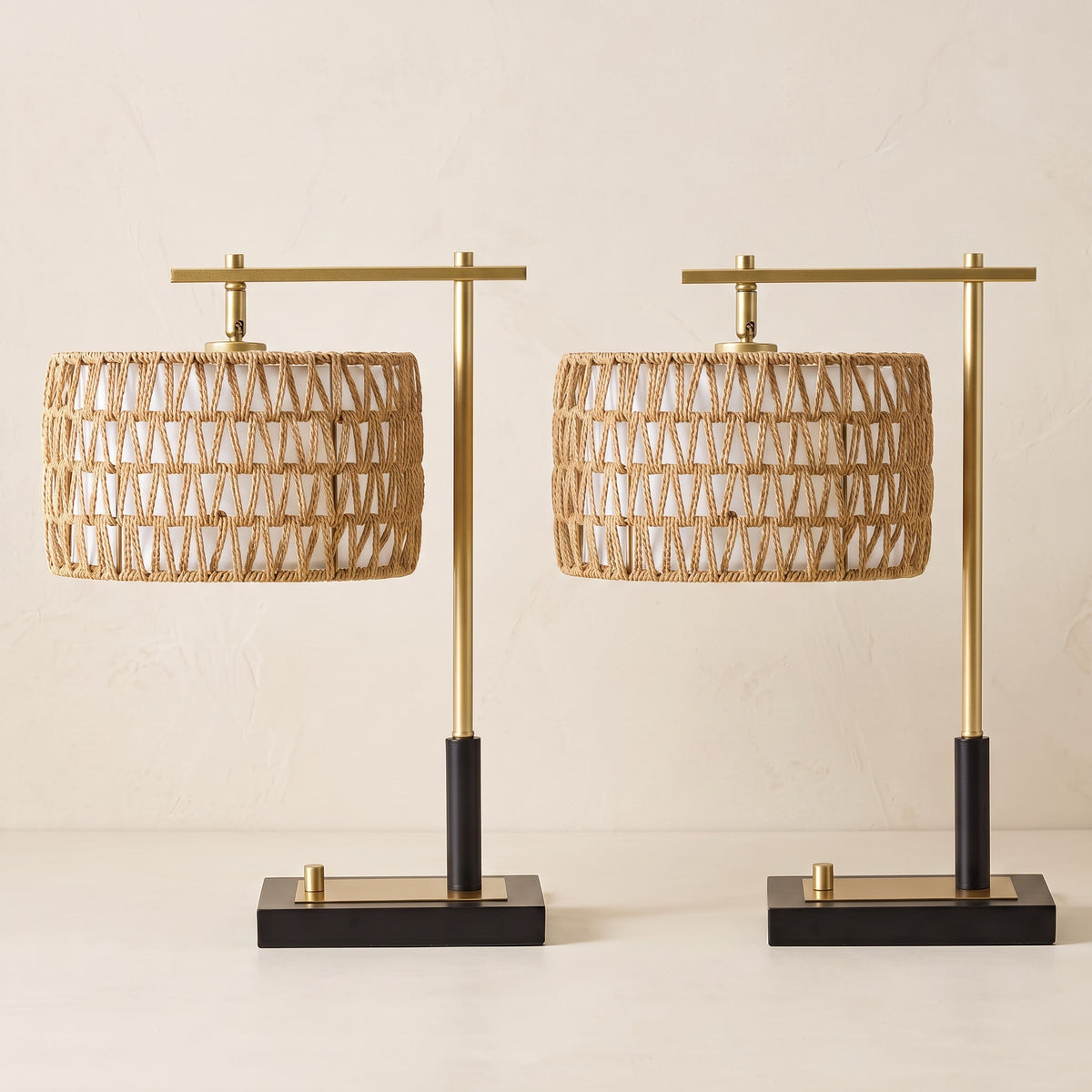 Pair of woven rope table lamps with gold arms and black bases on an ivory plaster backdrop