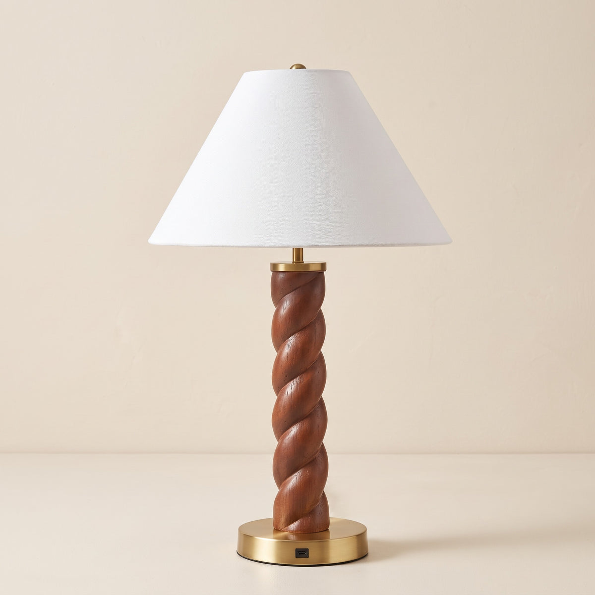 Twisted wood-look table lamp with white empire shade and brass base with USB-C port on an ivory backdrop