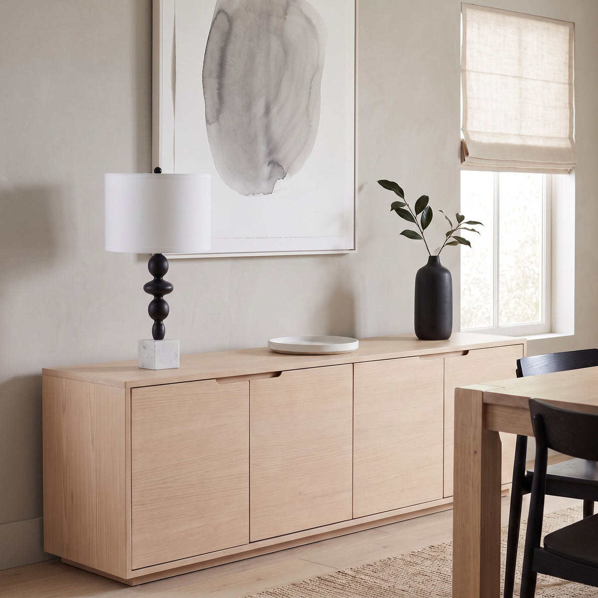 Black tiered table lamp with white marble cube base and white drum shade on a light oak sideboard