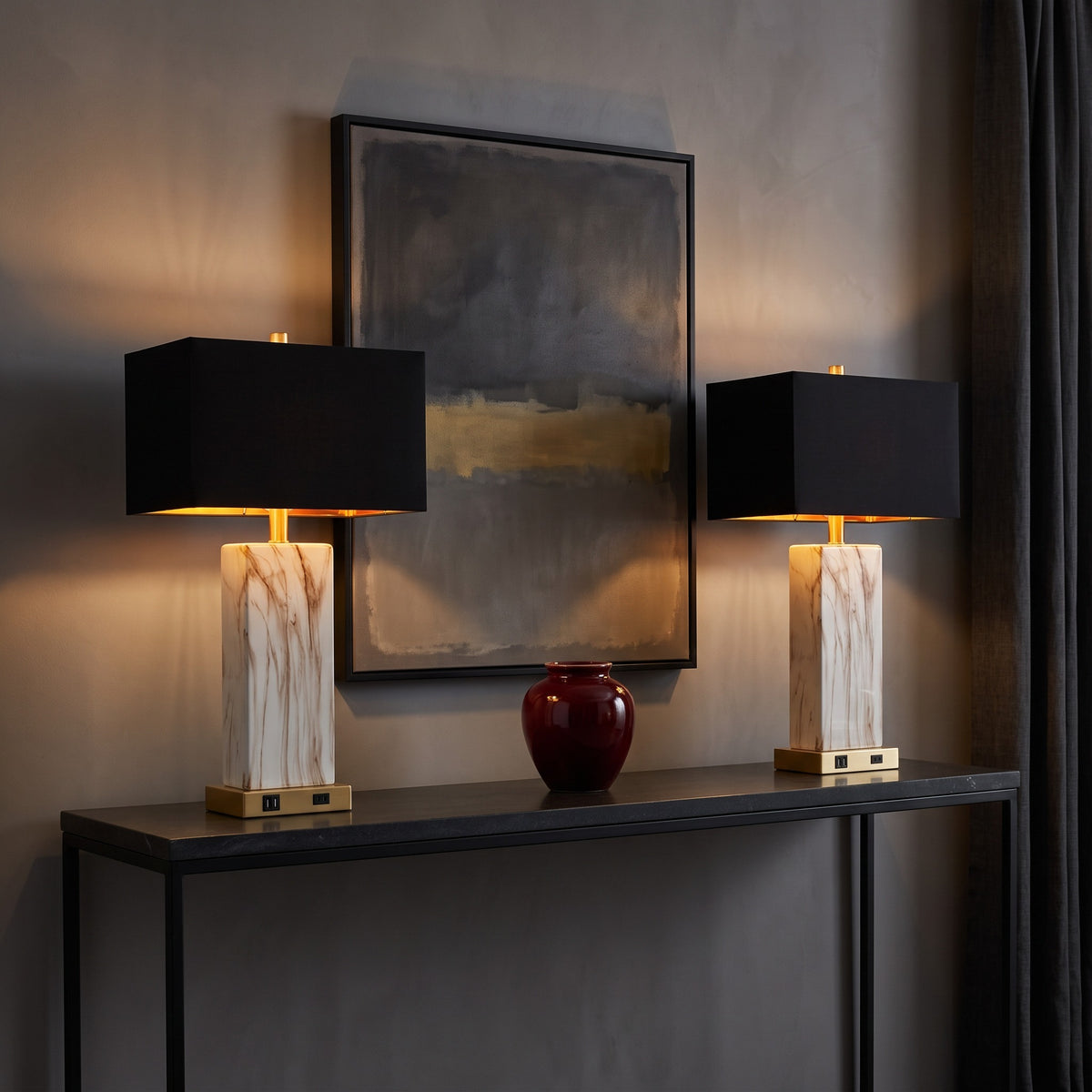 Pair of white marble-look table lamps with black shades and gold bases, lit on a black console table