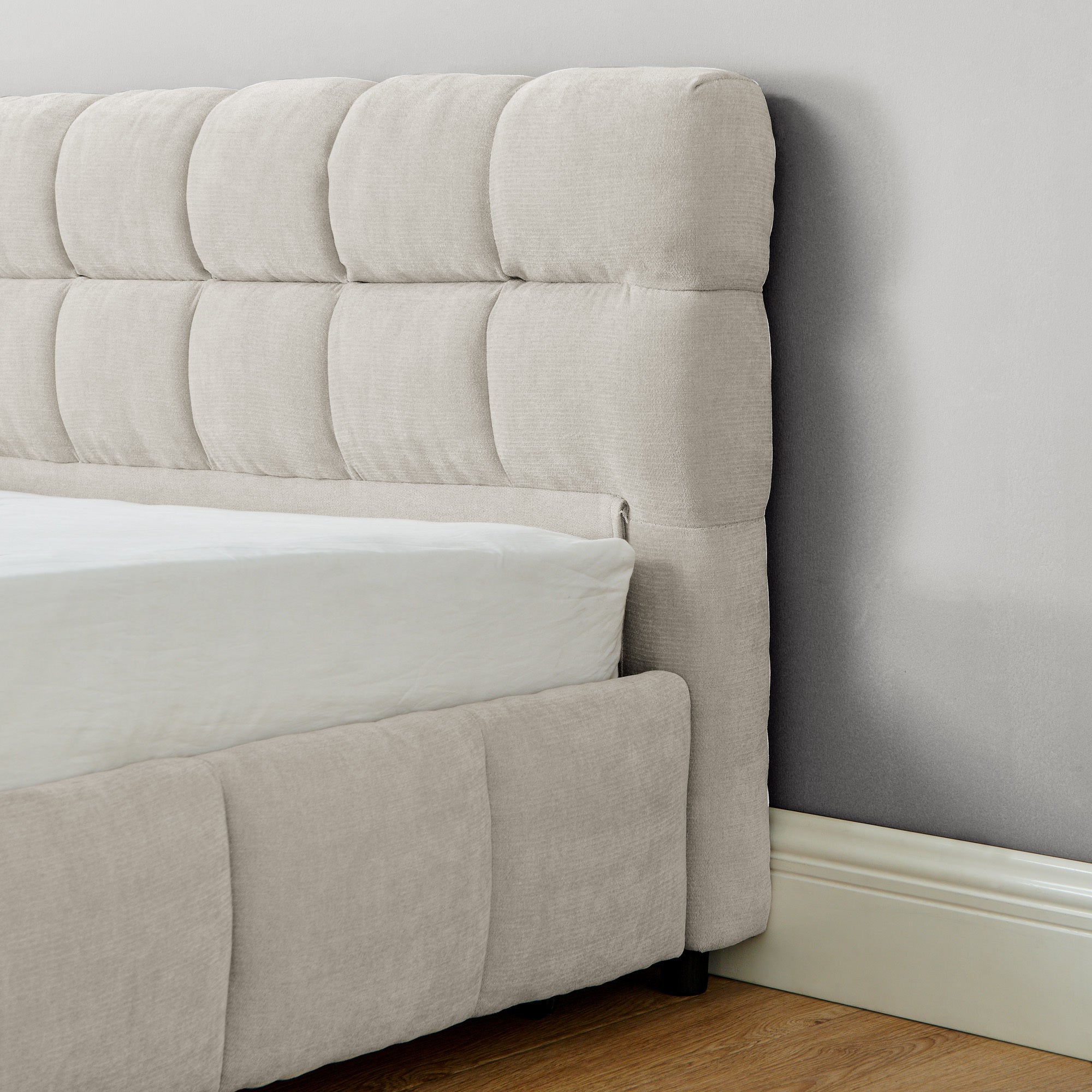 Close-up of tufted beige chenille headboard corner near wall