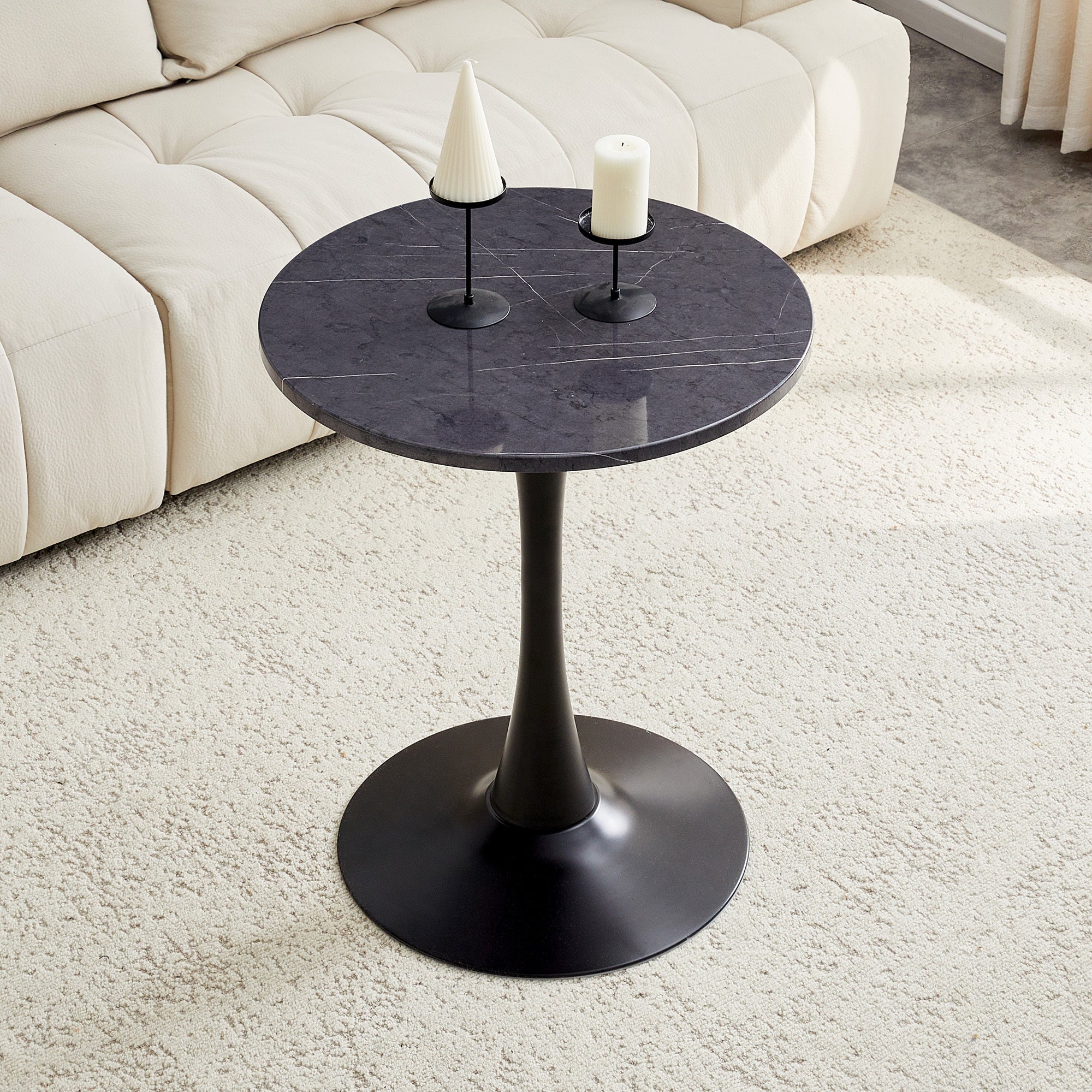 Black marble-look bistro table with two candle holders beside a cream tufted sofa, high angle view