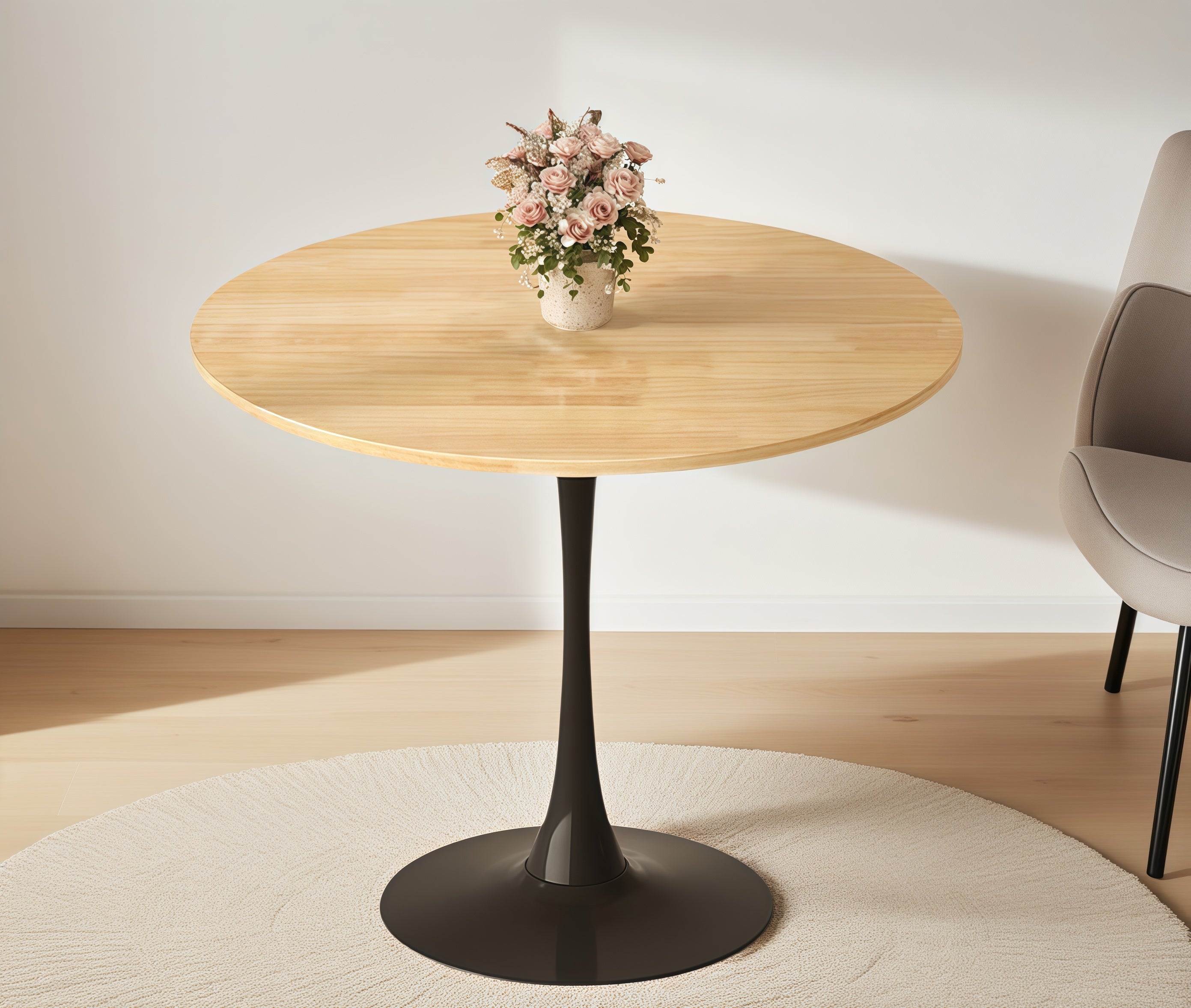 Natural wood round bistro table with pink flowers beside a beige upholstered chair on a wood floor