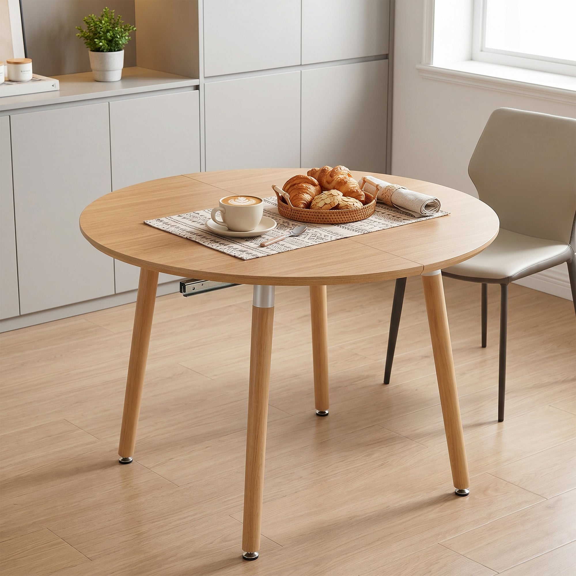 Oak-look round dining table styled in a kitchen with coffee and croissants, three-quarter view