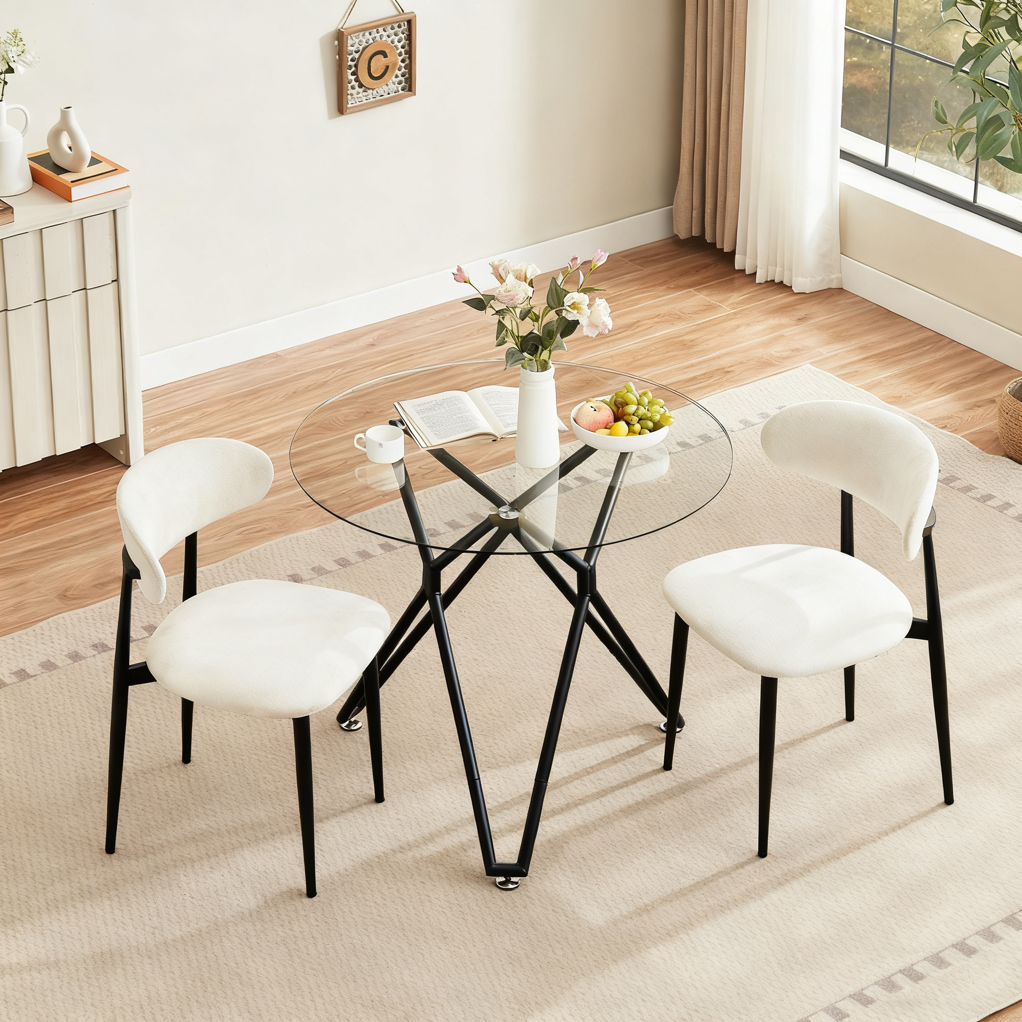 Overhead view of the round glass dining table with two cream boucle chairs, flowers and fruit in a dining nook