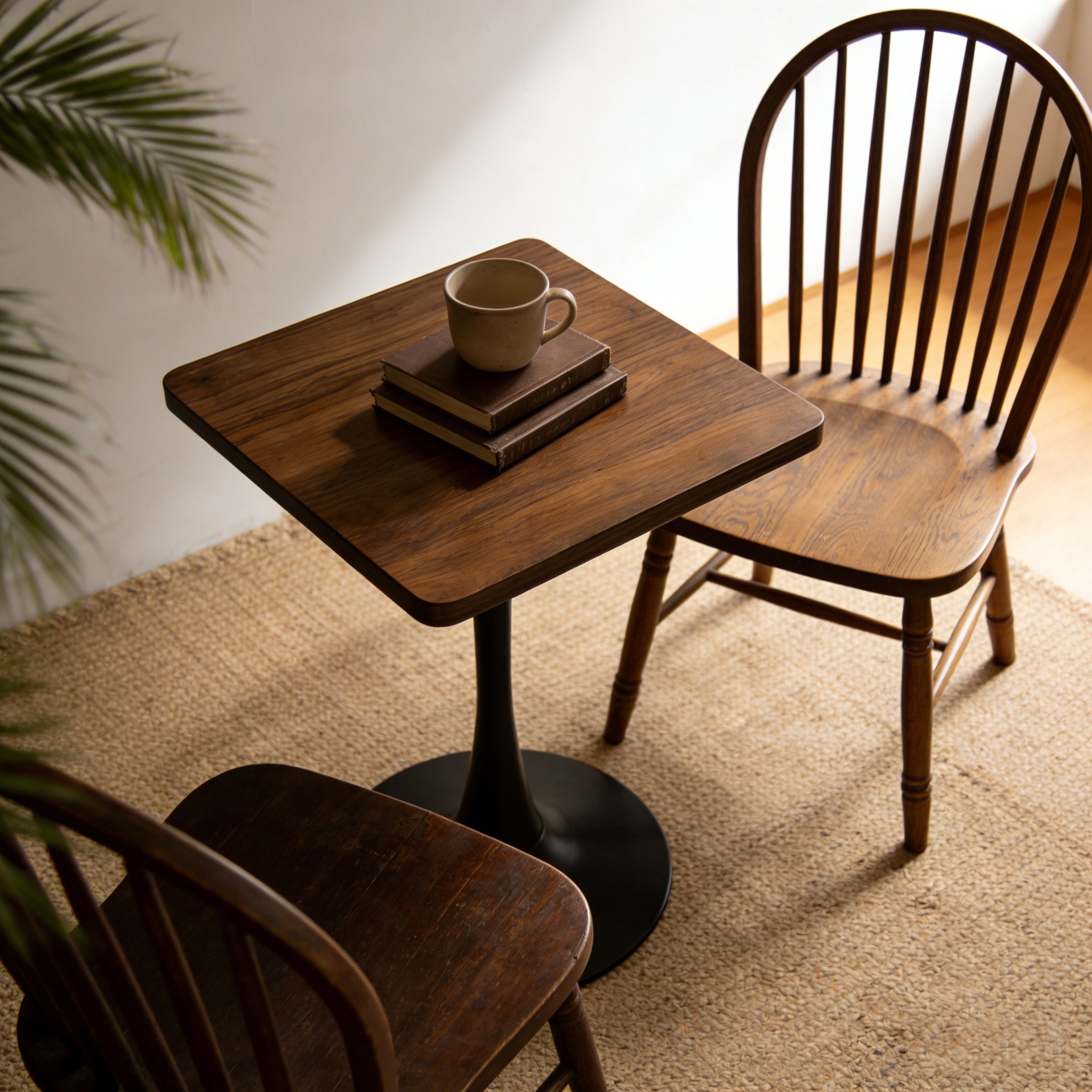 Overhead view of walnut square tulip bistro table styled with a mug and books beside a wooden chair on a jute rug