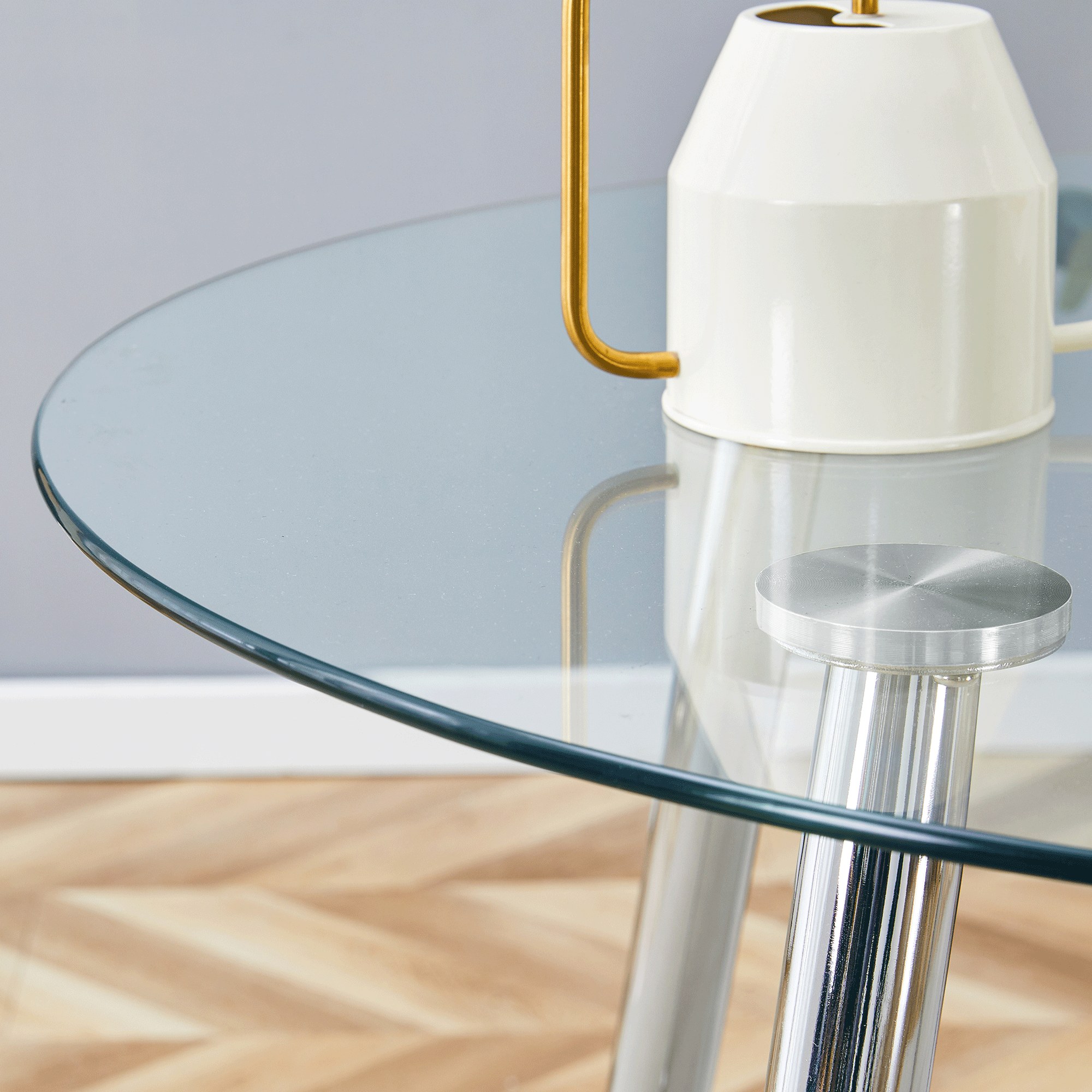 Close-up of the glass table edge and silver leg top with a cream vase on the surface