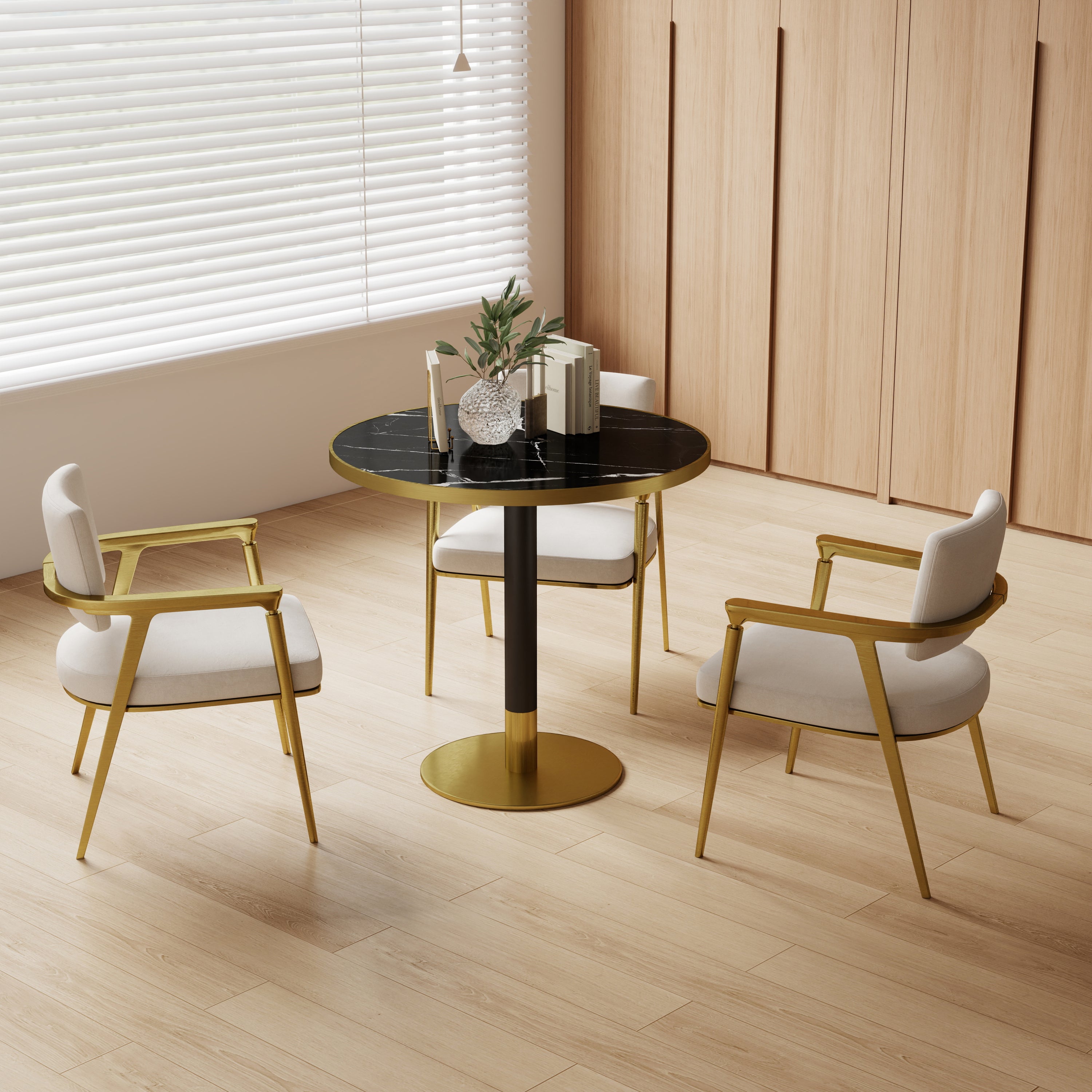 Black and gold round dining table styled in a bright room with two cream chairs and books on a wood floor