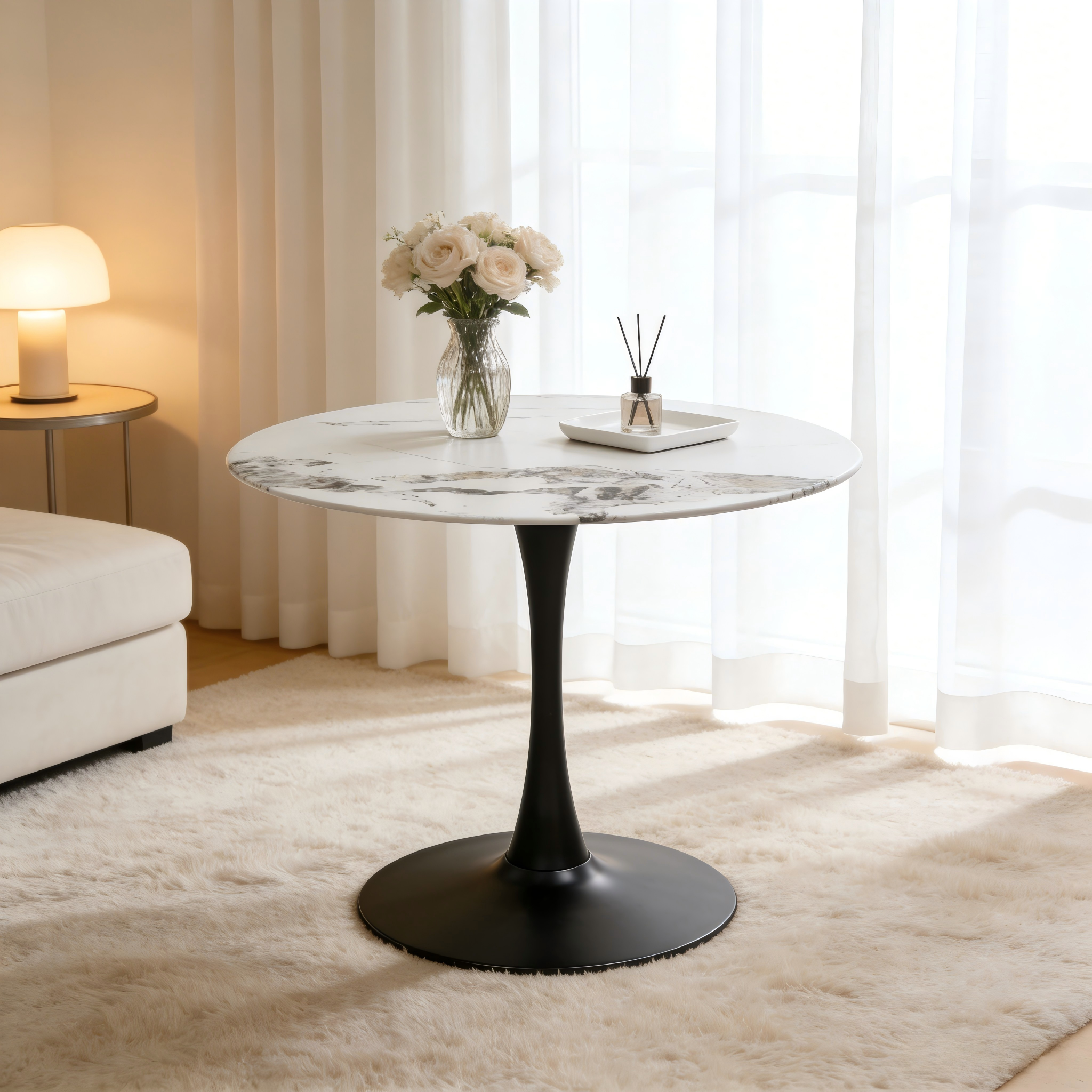 Faux marble tulip dining table with black pedestal styled with roses beside a lamp