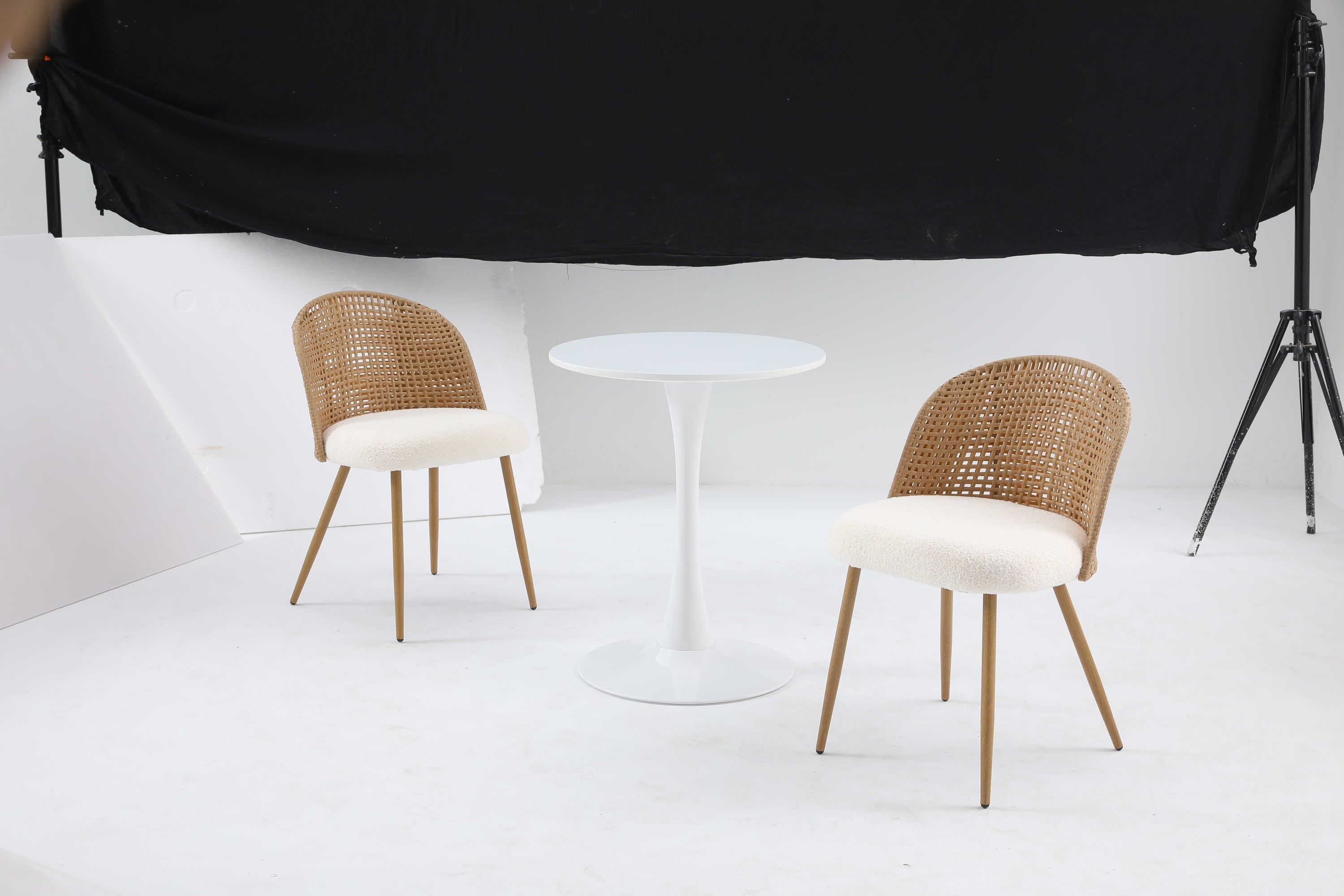 White round bistro table between two rattan and boucle chairs in a photo studio