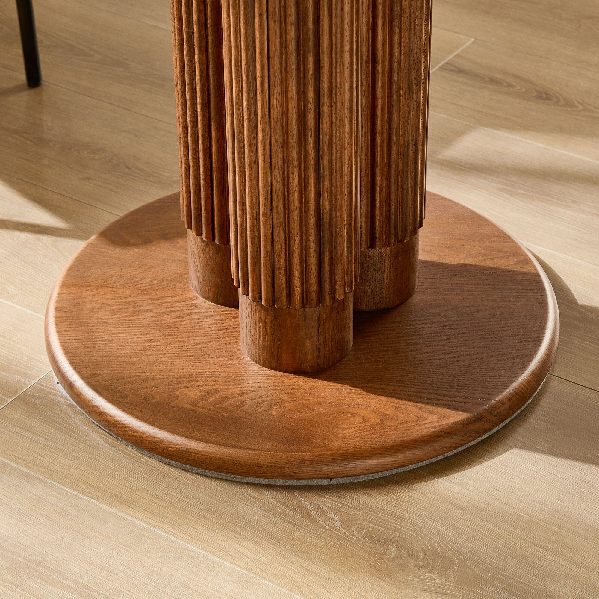 Close-up of the fluted wood pedestal on its round base above light flooring