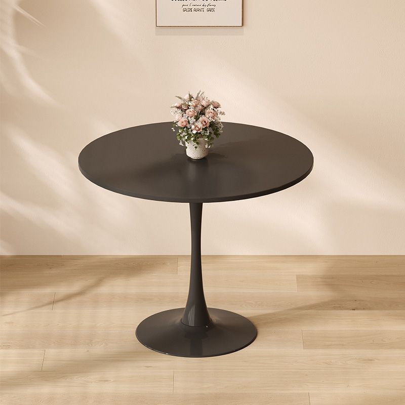 Black round dining table against a beige wall with framed art, holding pink flowers