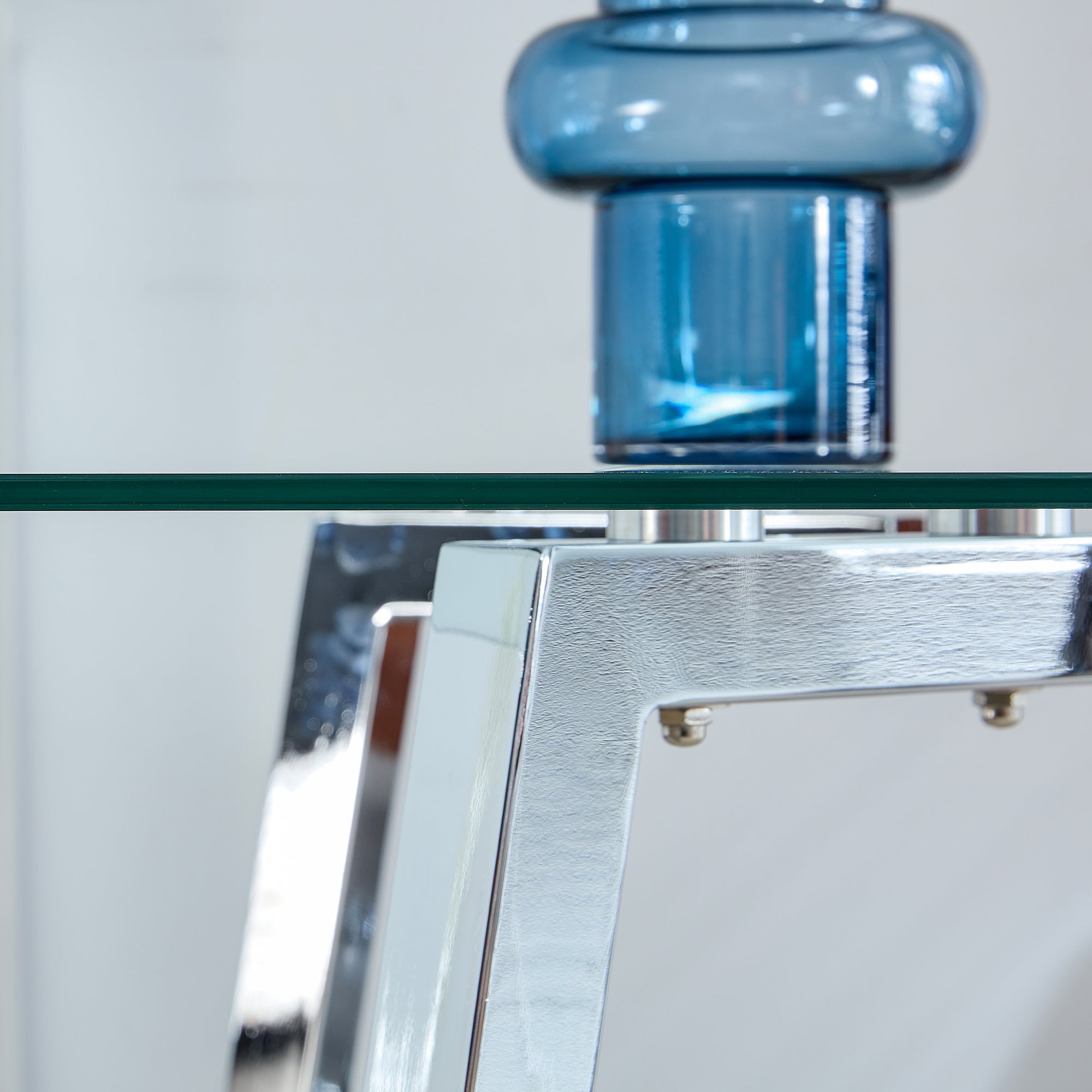 Close-up of the glass edge and chrome corner mount with round bolts, blue vase above