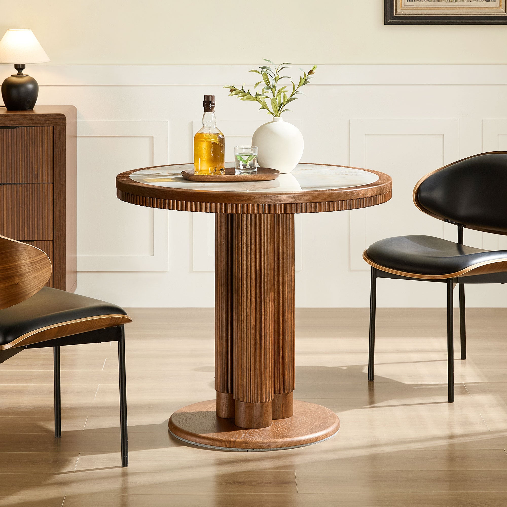 Round walnut dining table with white stone top and fluted pedestal, styled in a paneled dining room