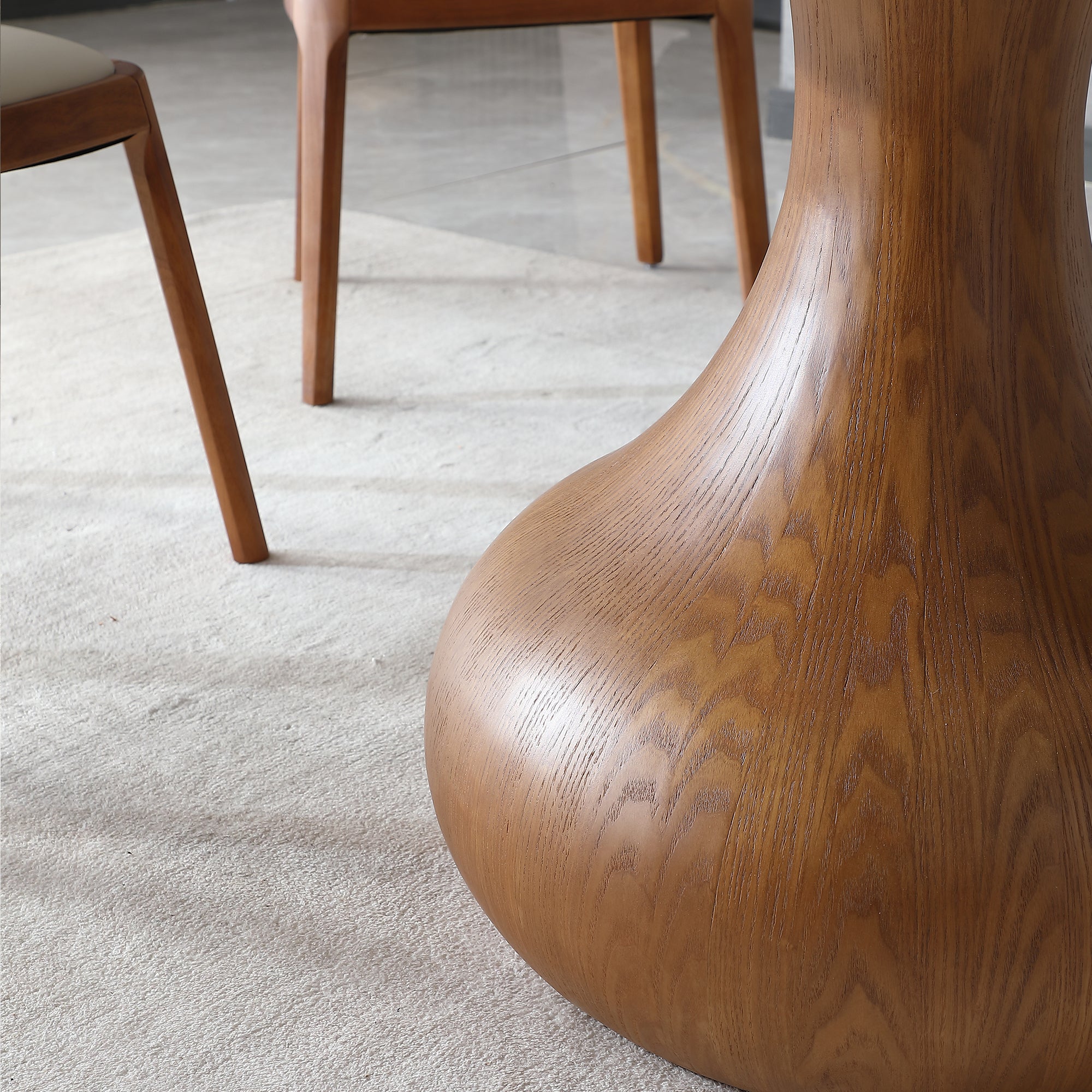 Close-up of the walnut-tone wood urn pedestal base of the round dining table on a rug