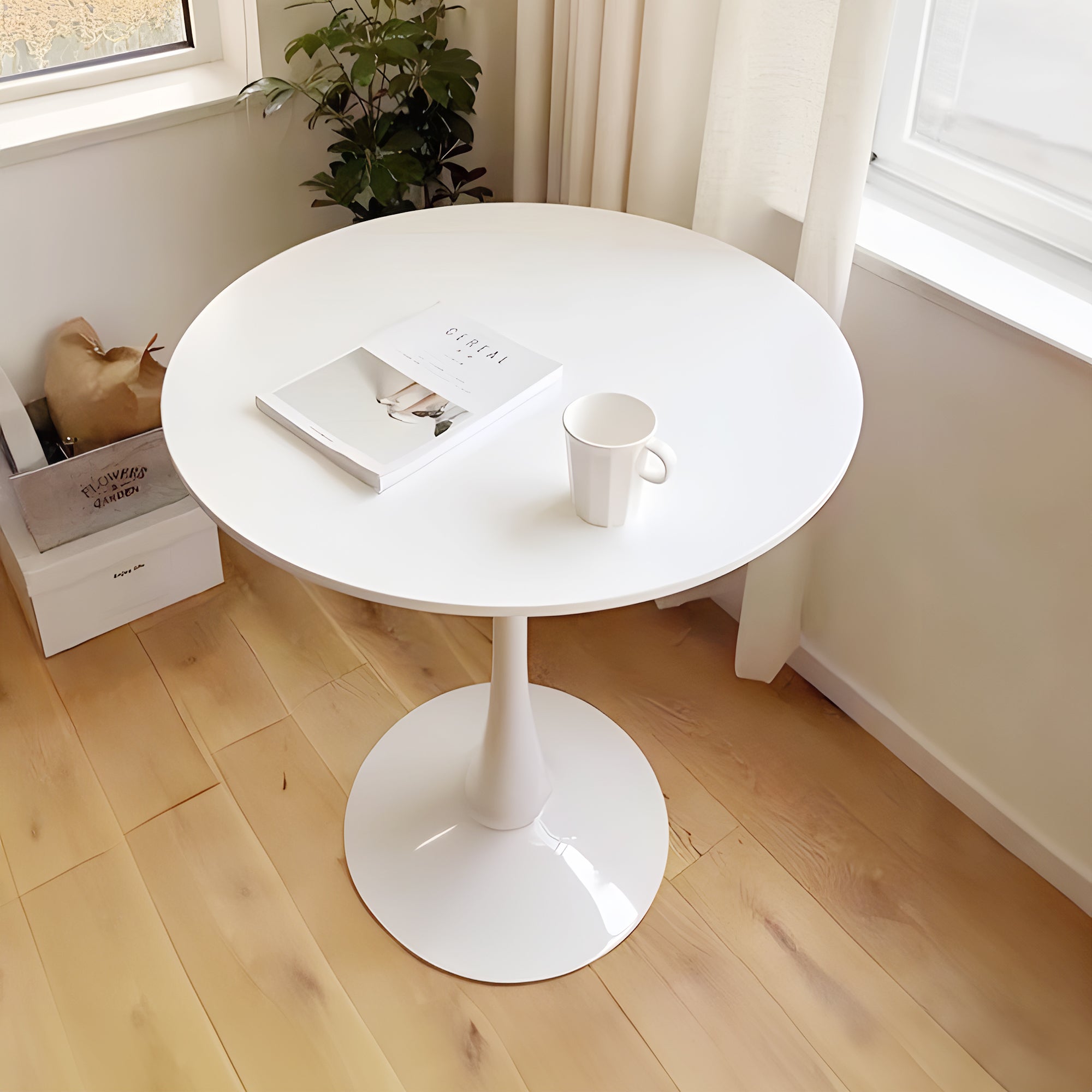 High angle of white tulip dining table in a bright room with a plant, holding a magazine and mug