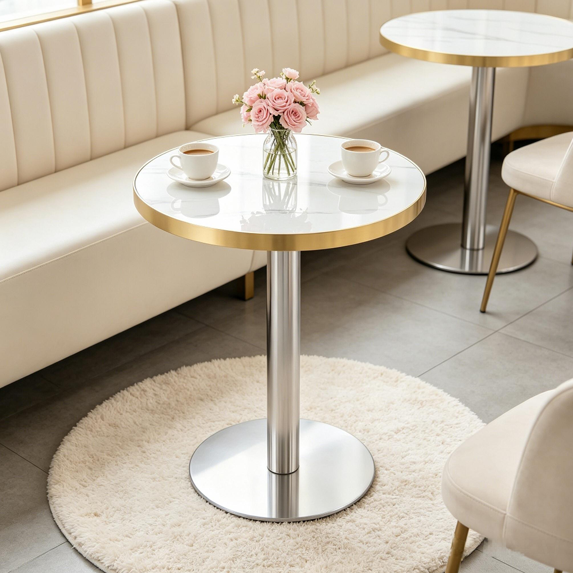 White faux marble bistro table with gold trim in a cream cafe booth beside a matching second table