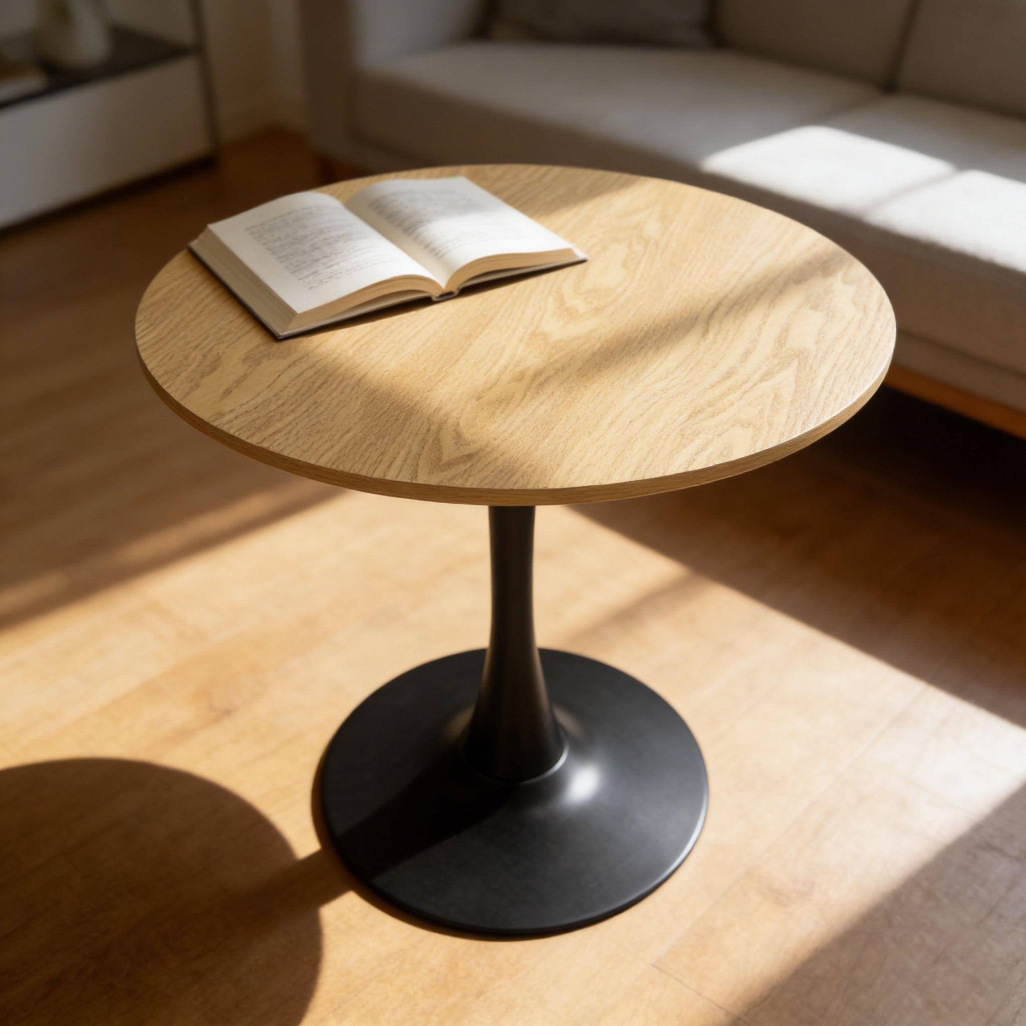 Three-quarter view of the natural round pedestal dining table in sunlight with an open book on top