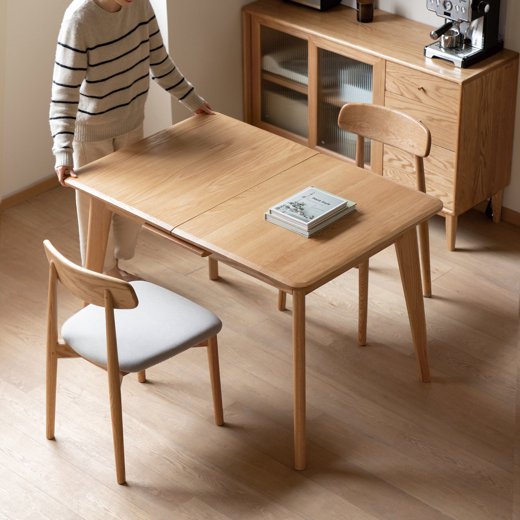 Woman pulling open the natural oak extendable table in a room with an oak sideboard and coffee machine