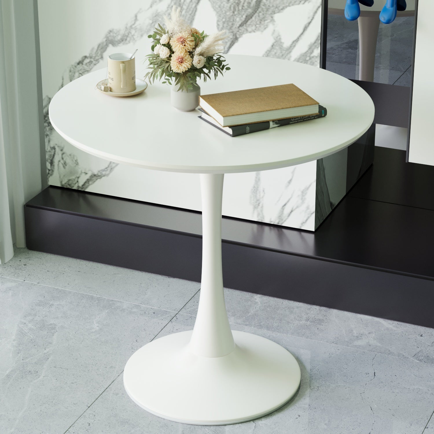 White round tulip dining table against a marble wall, topped with a mug, vase, and books