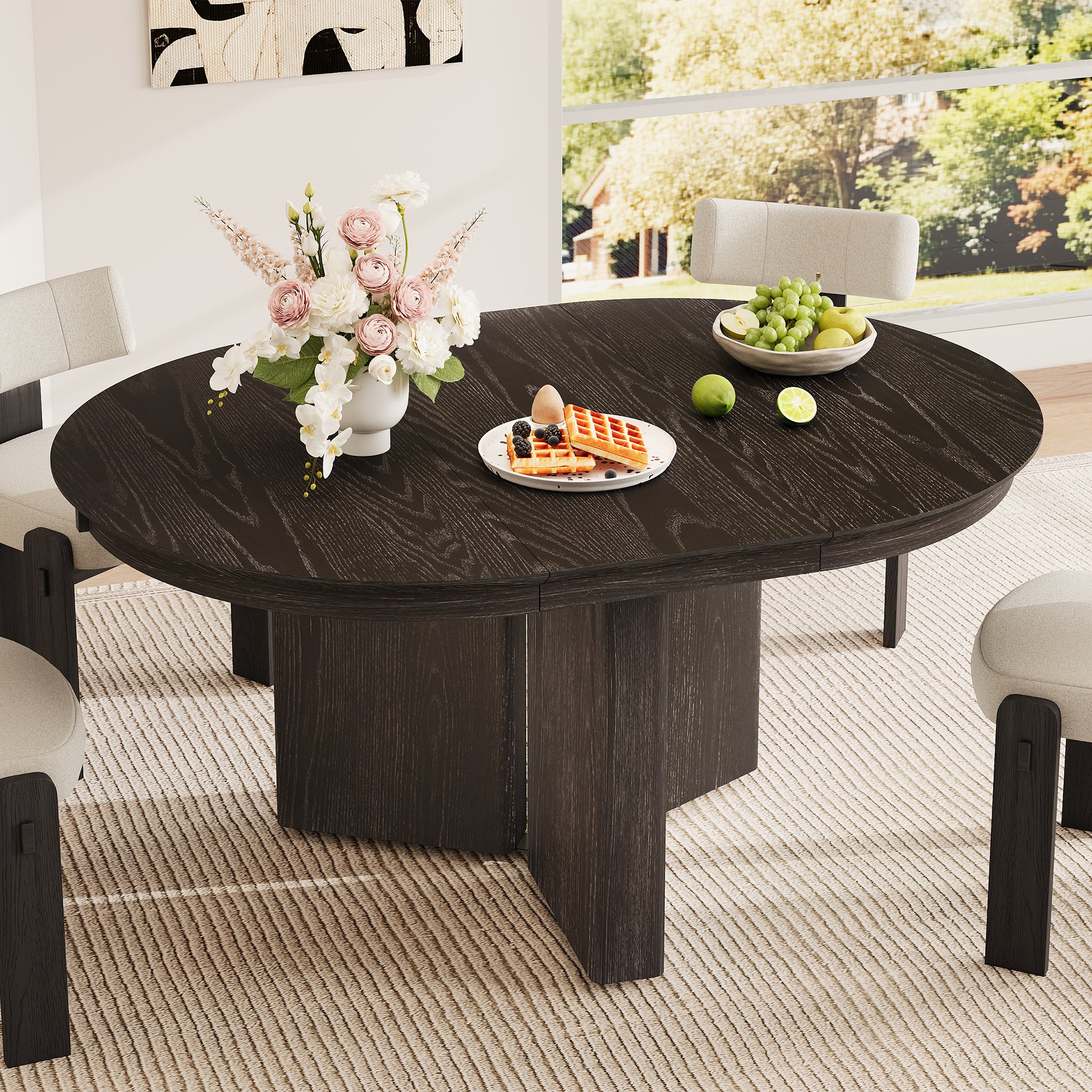 Round espresso table styled with flowers, waffles and grapes among cream chairs by a window