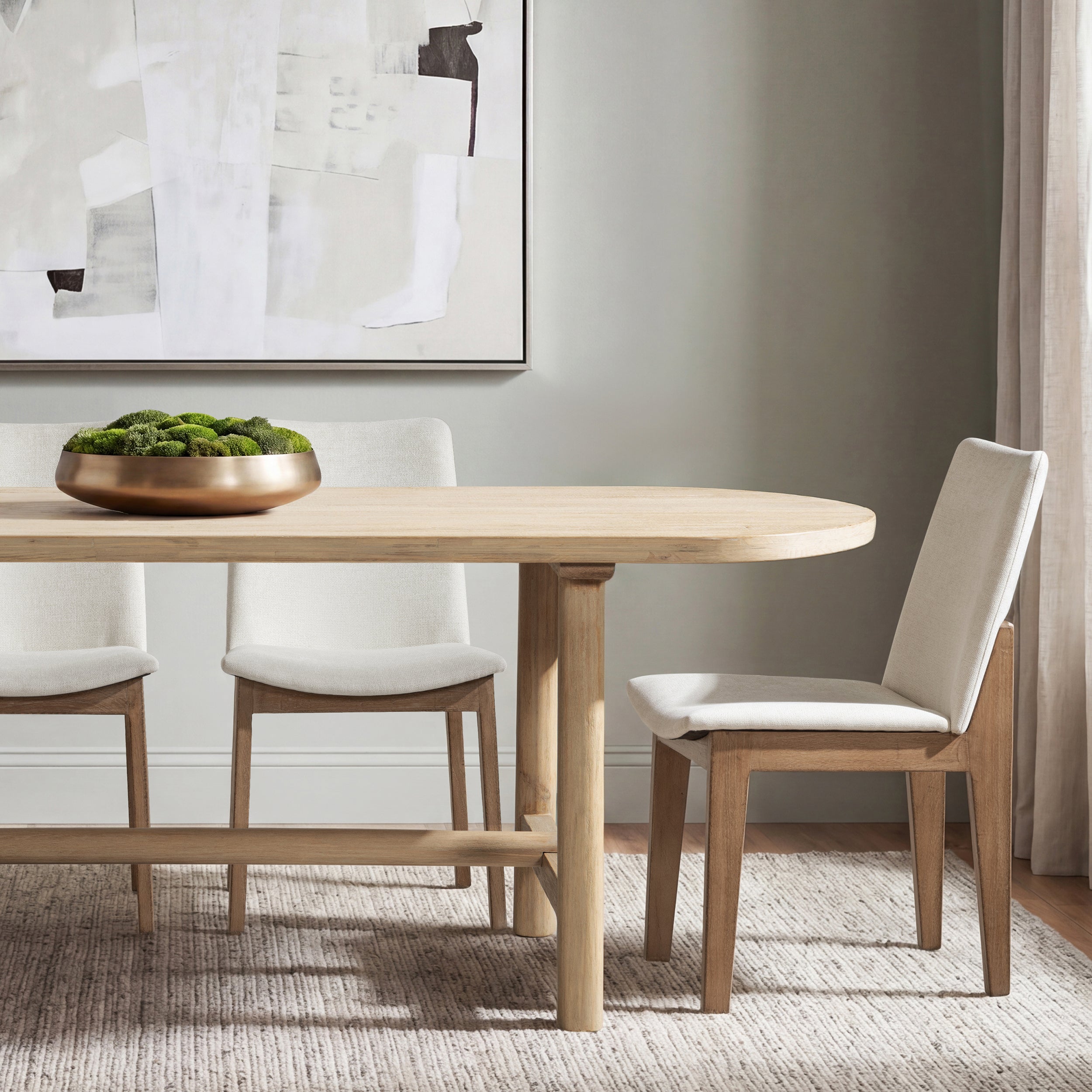Cerused pine oval dining table styled with cream chairs and a moss centerpiece