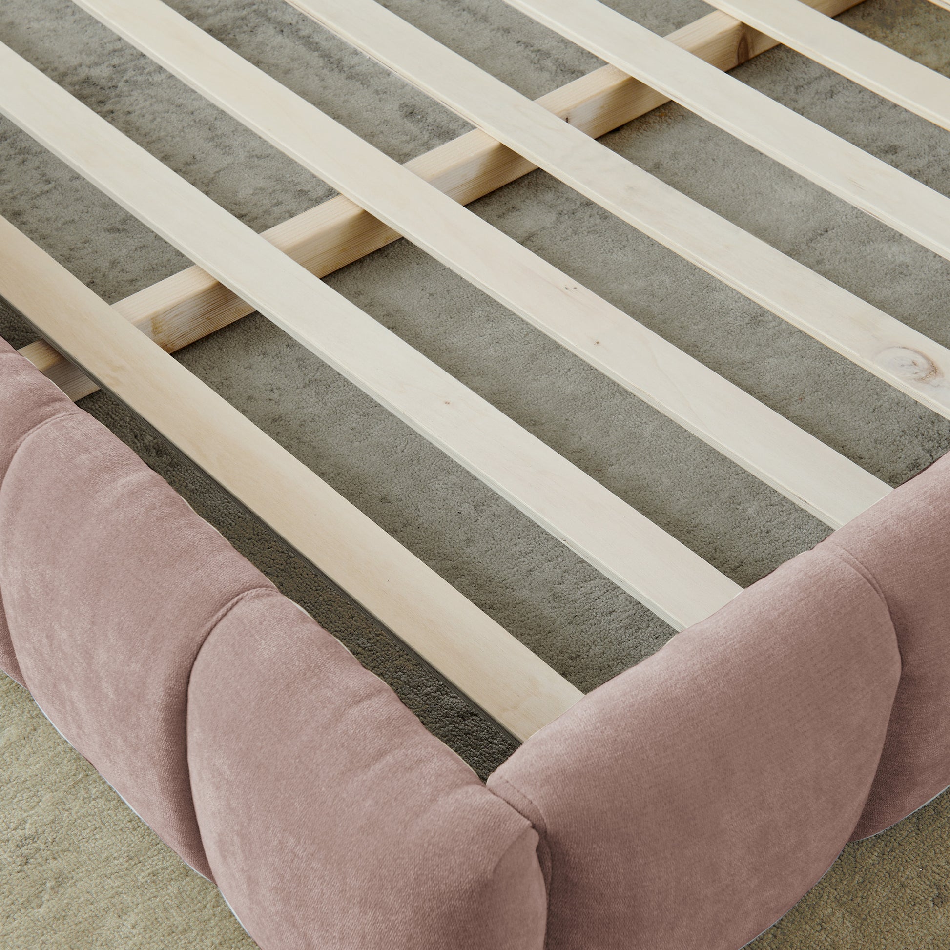 Overhead view of wood slats and pink upholstered frame rail, no mattress