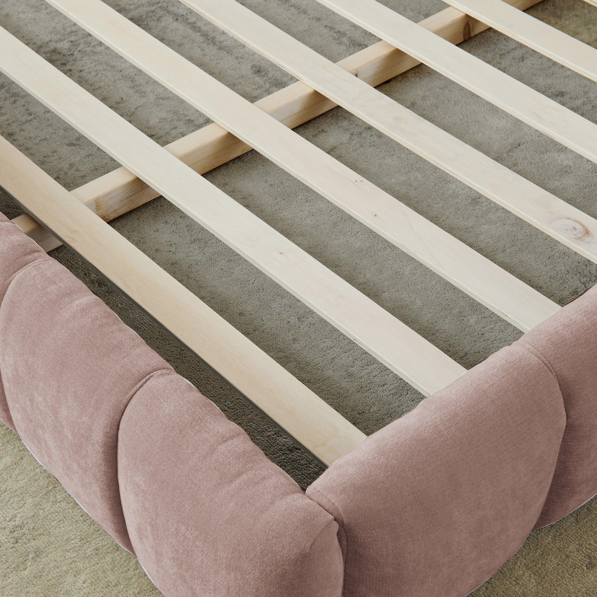 Overhead view of wood slats and pink upholstered frame rail, no mattress