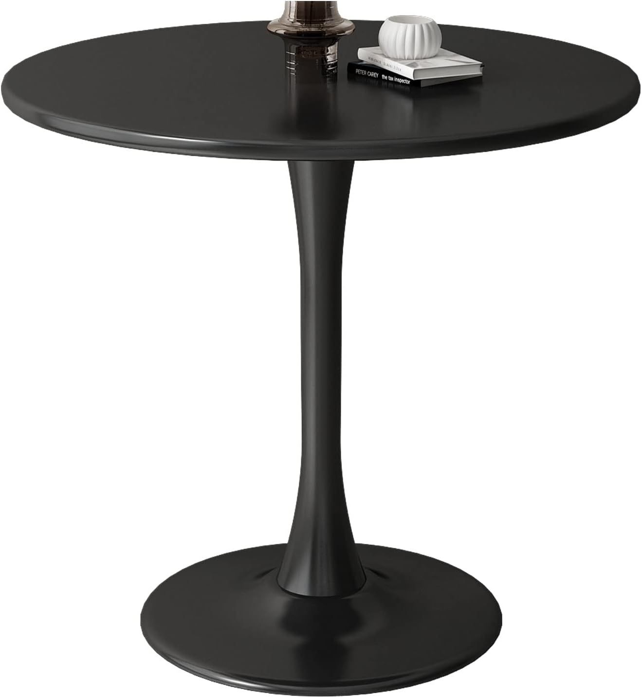 Black round dining table on a white background styled with a glass vase, book, and ornament
