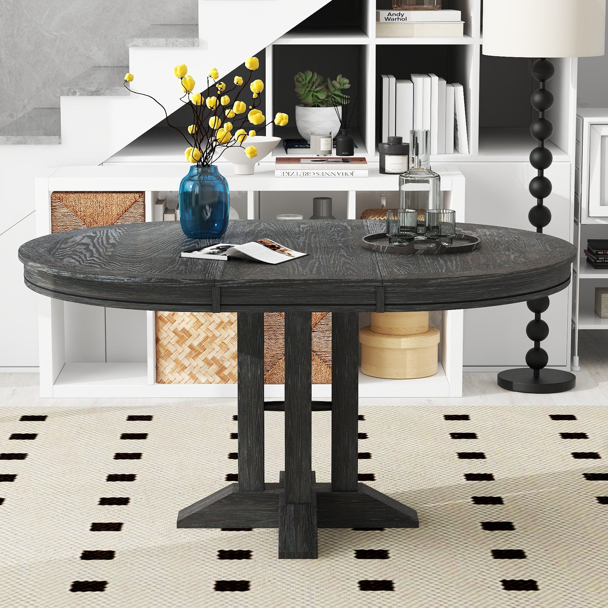 Black farmhouse dining table extended to an oval, three-quarter view in a styled room with shelving