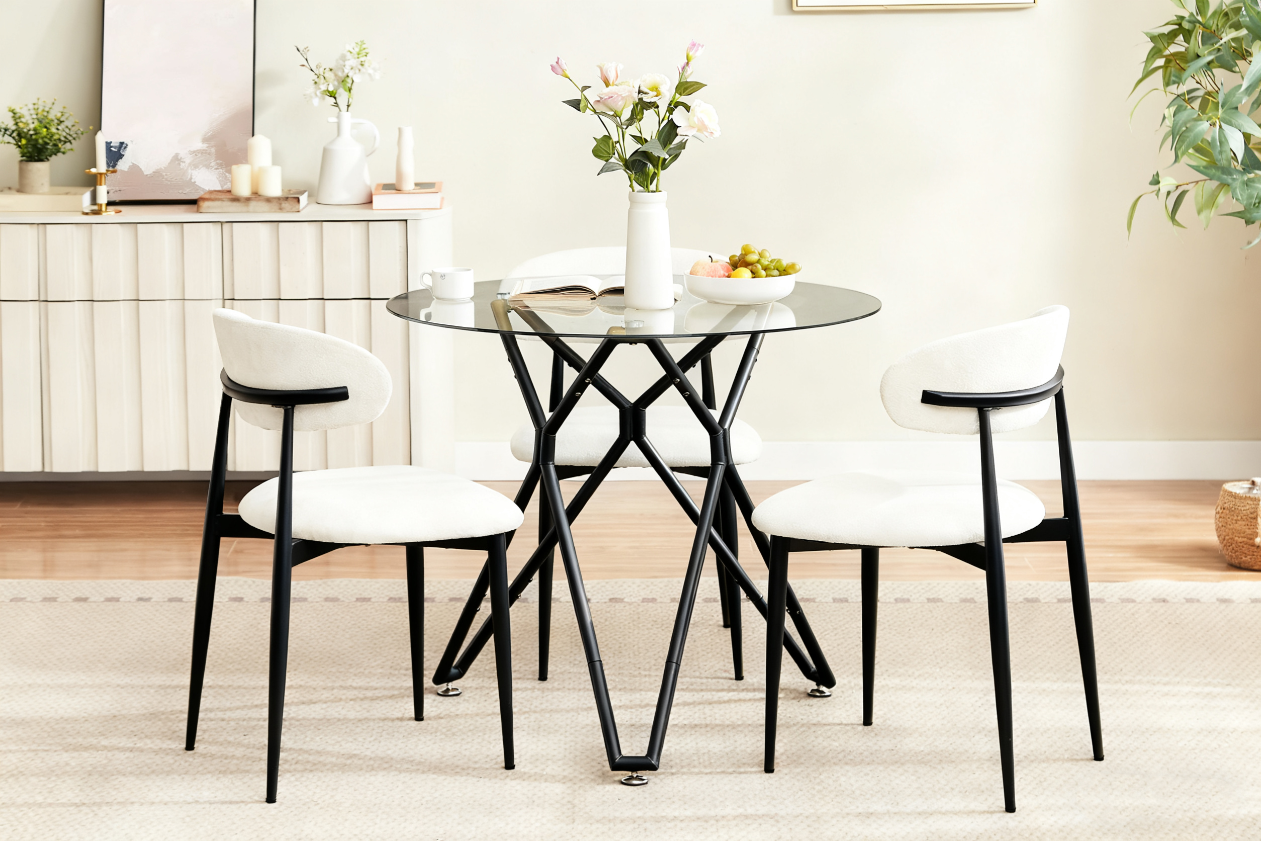 Round glass dining table with three cream boucle chairs beside a fluted sideboard