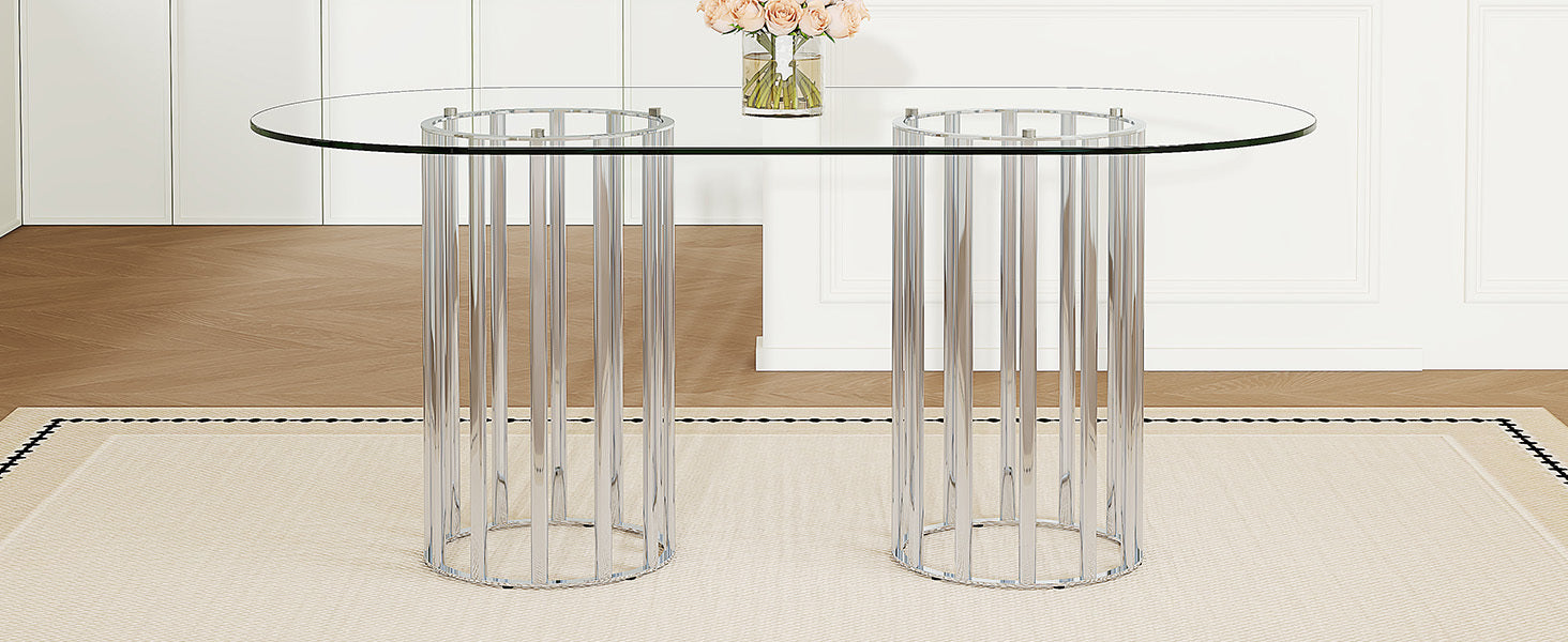 Oval glass dining table with silver double-column base in a white paneled room.