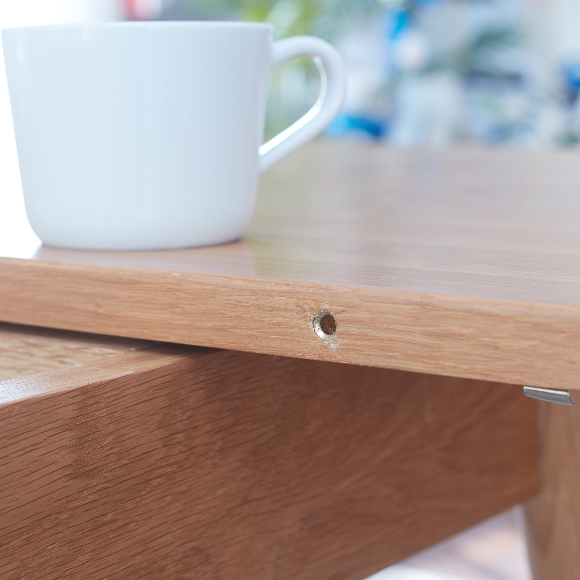 Close-up of the oak table edge showing a metal alignment pin hole, white cup on top