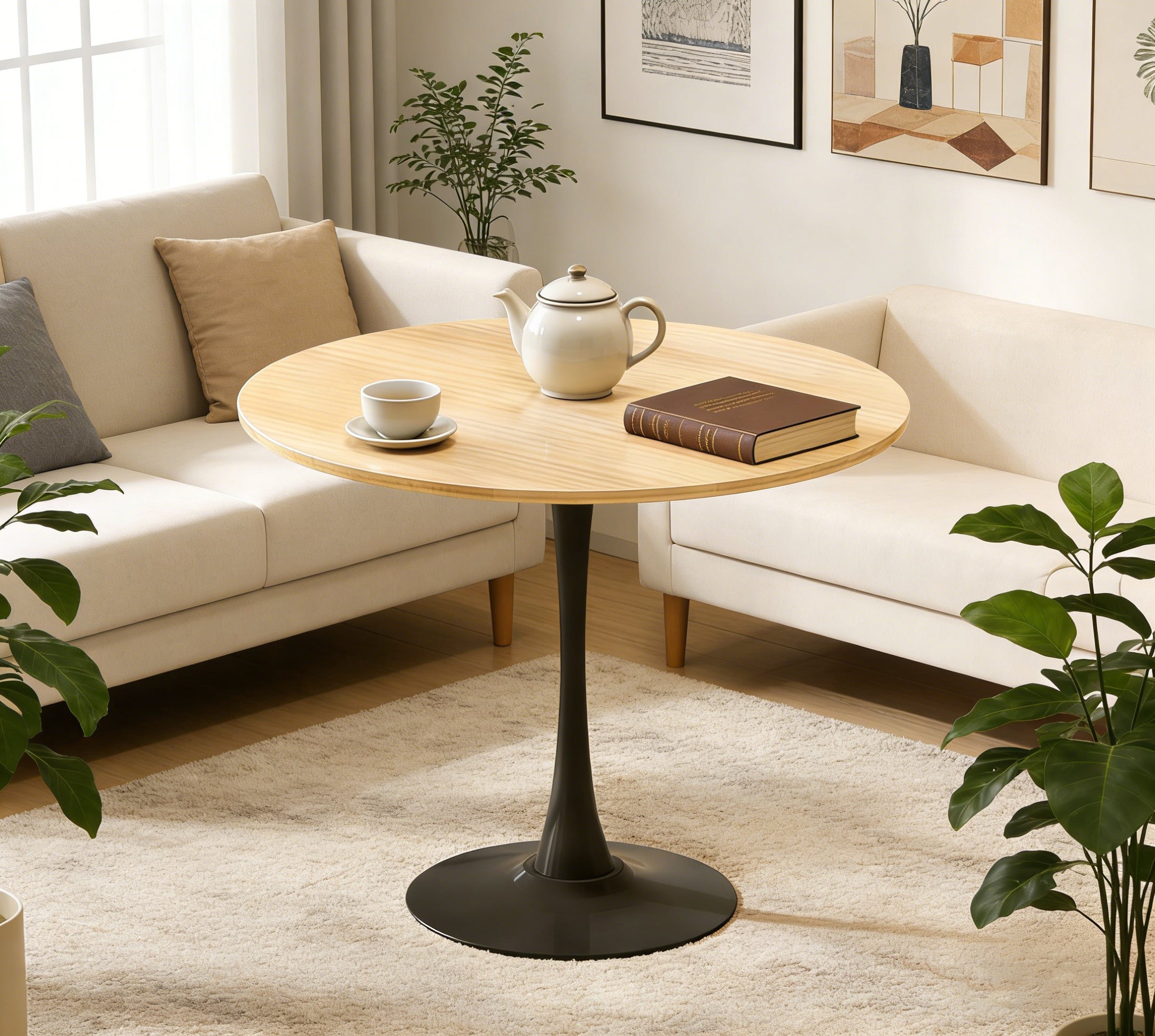 Natural round pedestal dining table styled in a living room with teapot, cup and book, cream sofas behind