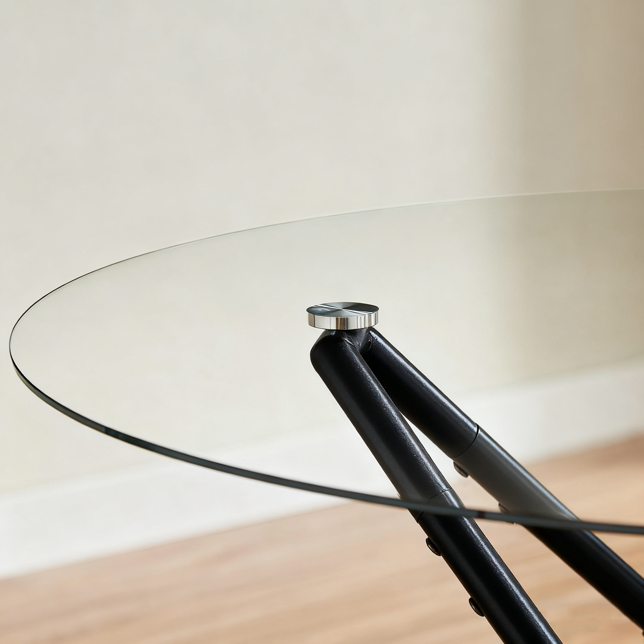 Close-up of the glass tabletop edge meeting a black leg with a chrome bolt cap