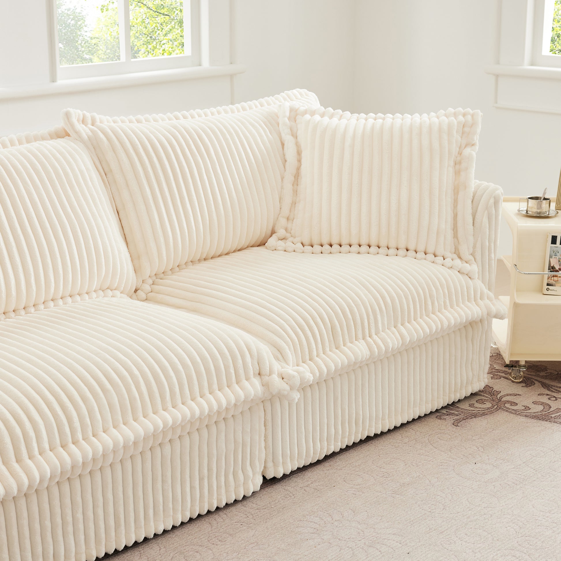 End of fluffy cream corduroy sectional highlighting overstuffed pillows, soft ribbed fabric, and cozy armrest detail.