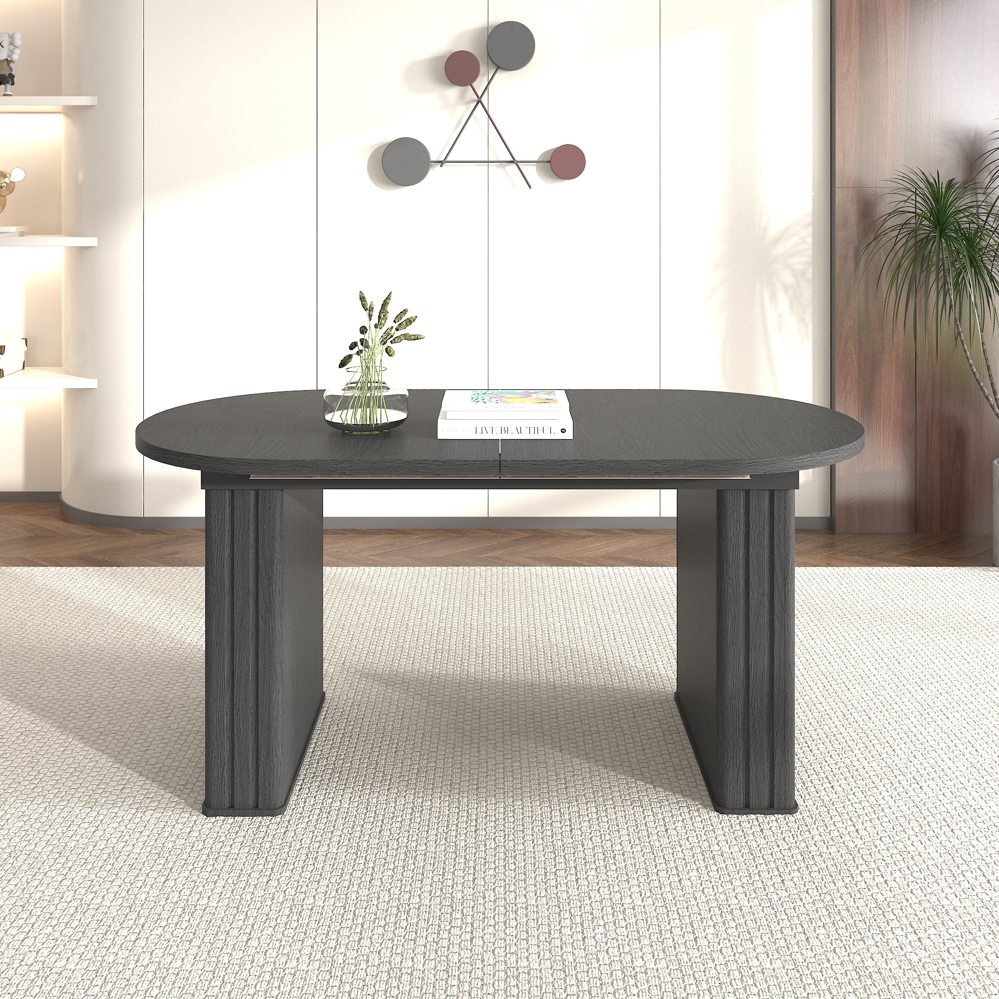 Black oval extendable dining table in a living room, front view with a glass vase and books on top