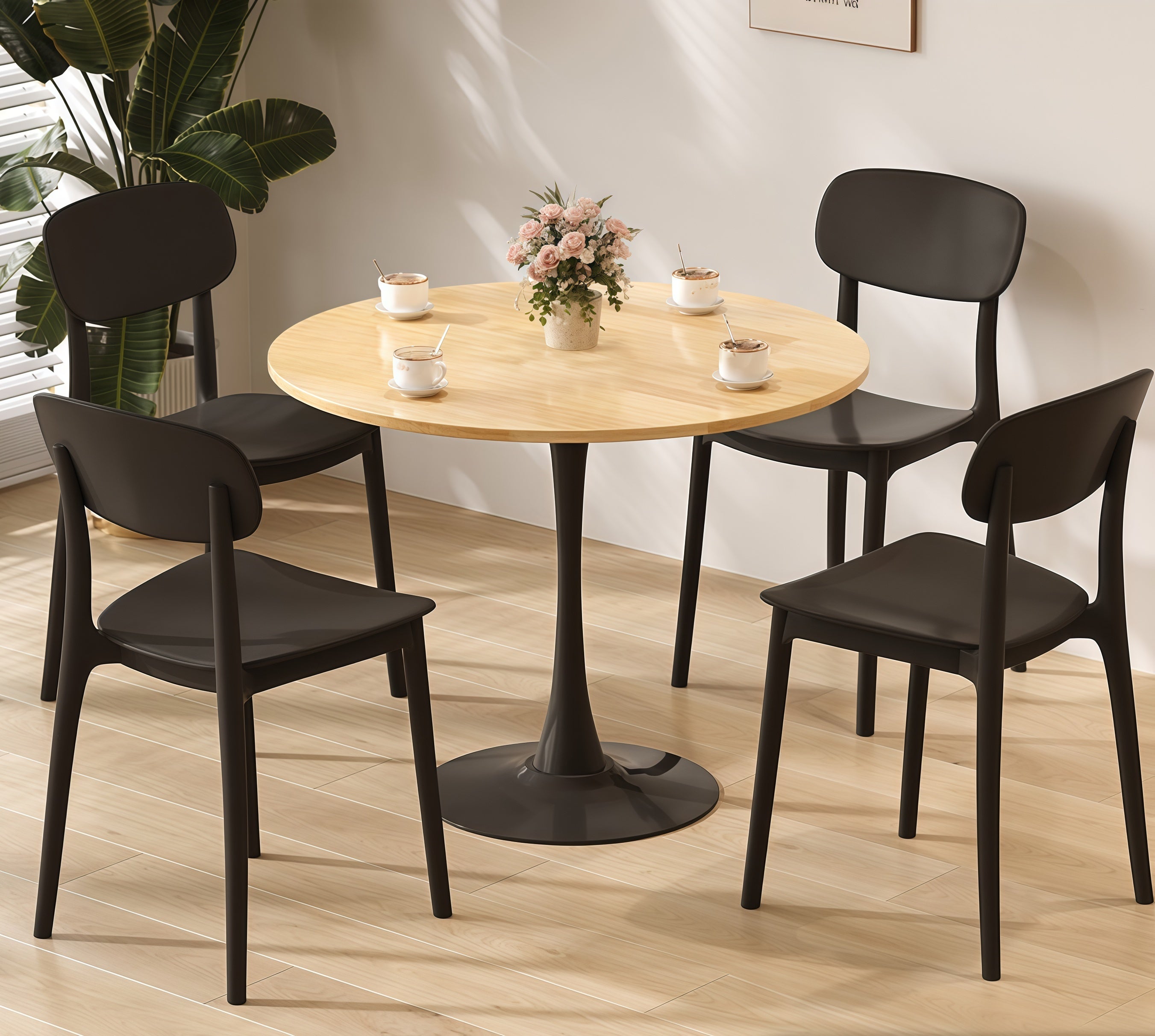 Natural wood round bistro table with black tulip pedestal in a styled nook with four black chairs and coffee cups