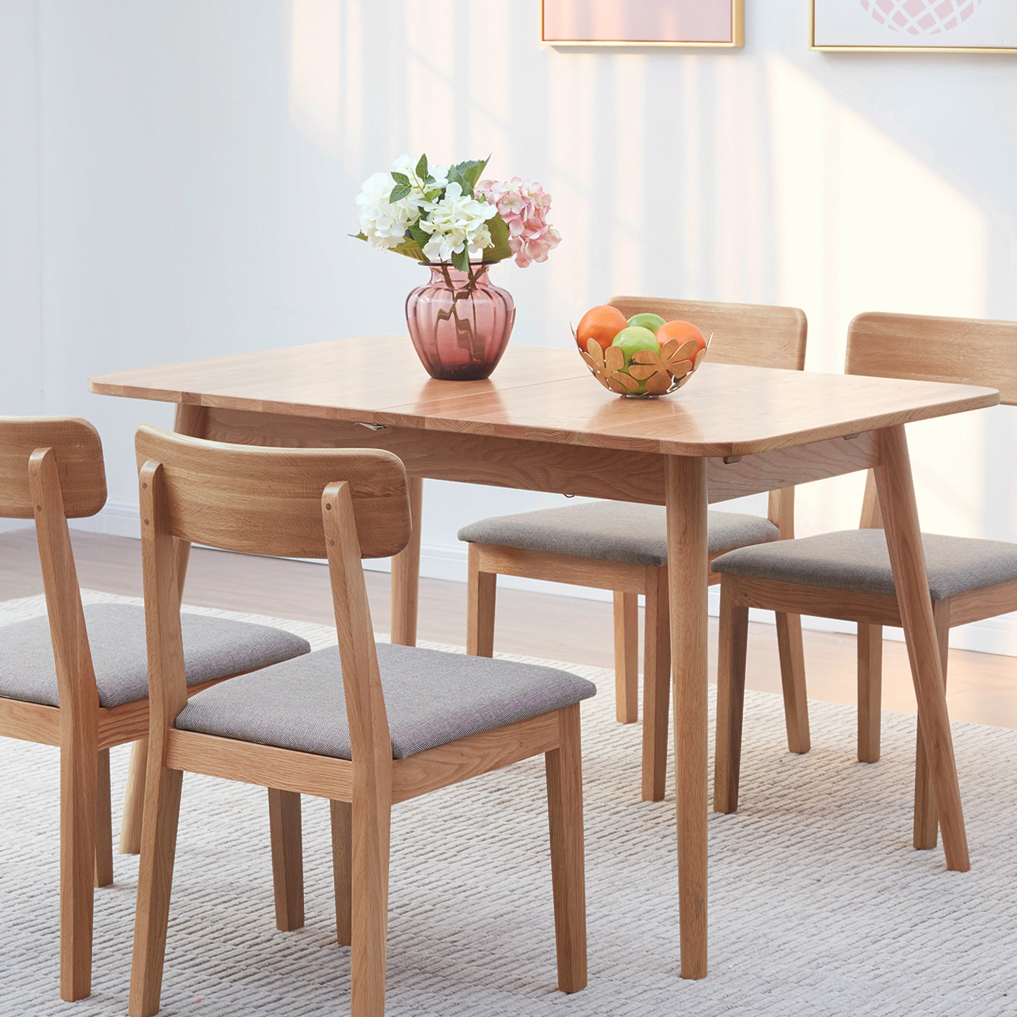 Natural oak dining table with oak chairs, a purple vase of hydrangeas and a fruit bowl in a bright room