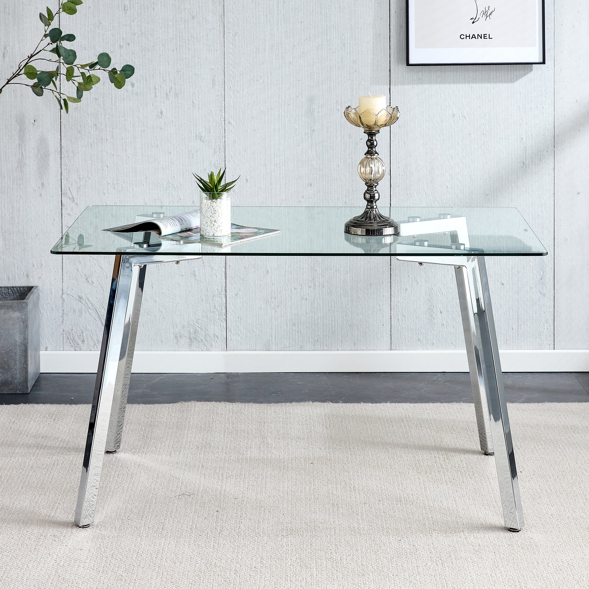 Front view of the rectangular glass dining table with chrome legs and a eucalyptus branch nearby