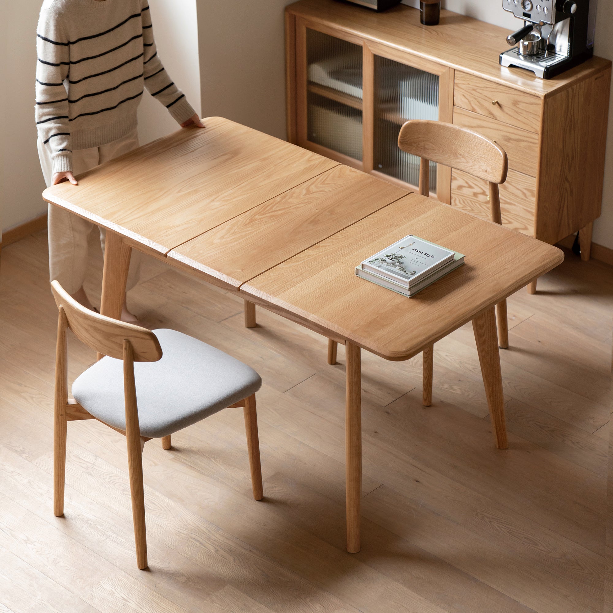 Natural oak dining table closed with a book and chairs in a bright room