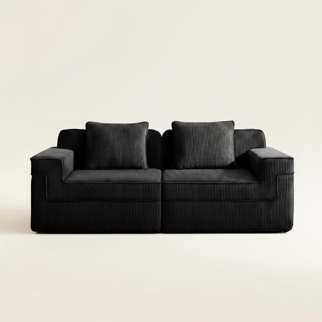 commercial photograph of the boneless couch in two seat format with black corduroy. picture shows the ridged texture of the corduroy upholstery and plush seating and pillows