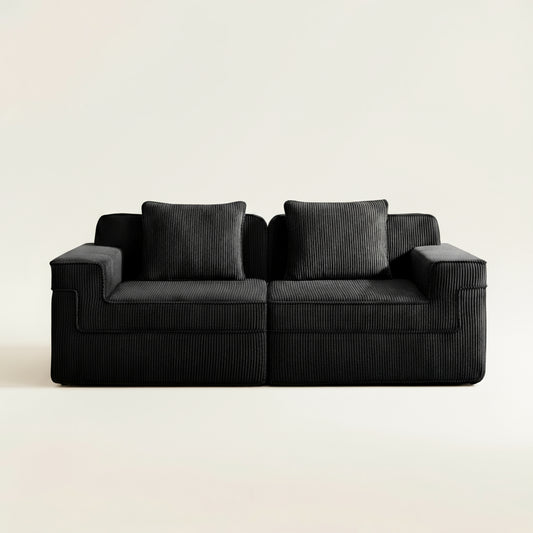 commercial photograph of the boneless couch in two seat format with black corduroy. picture shows the ridged texture of the corduroy upholstery and plush seating and pillows