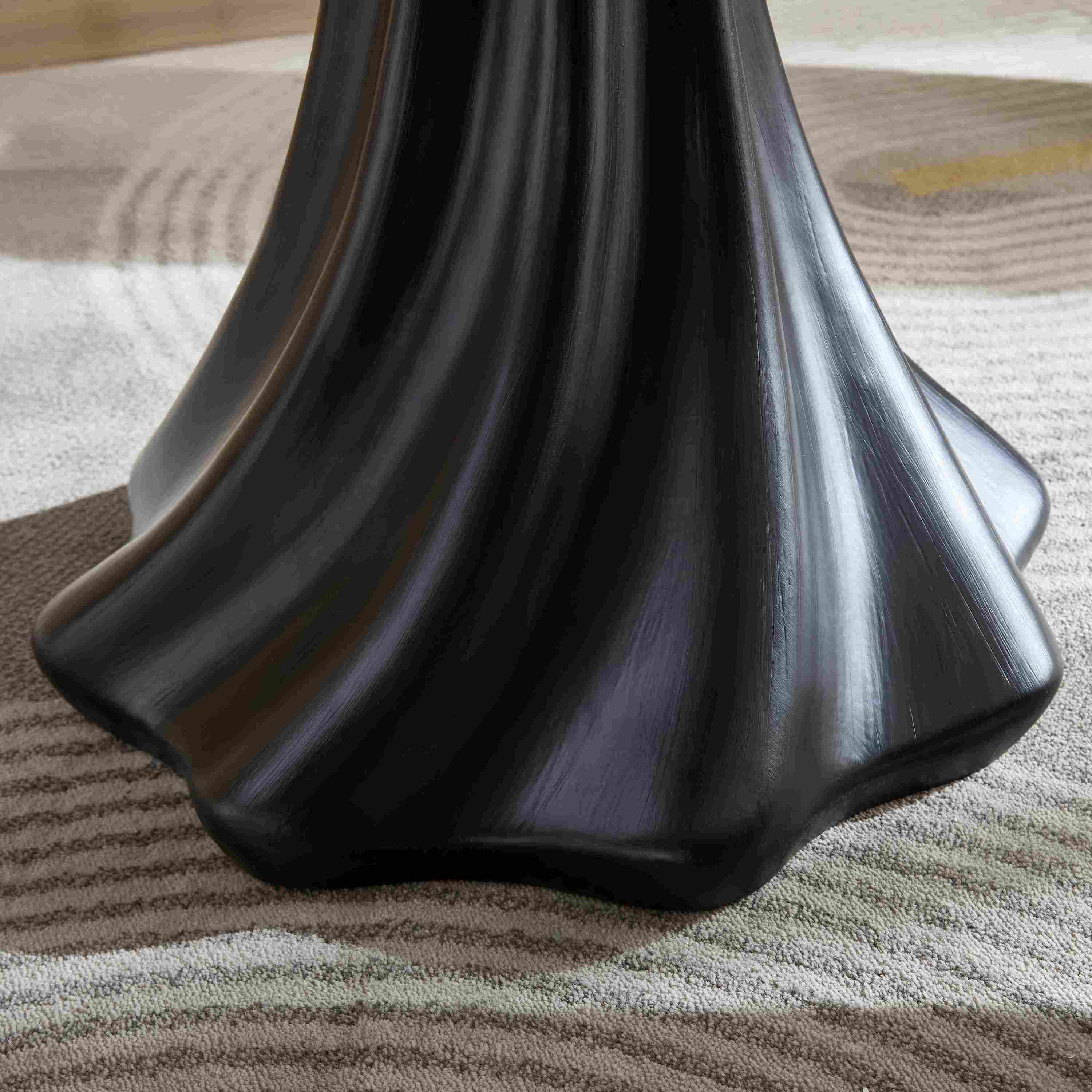 Close-up of the flared black fluted pedestal base of the petal dining table on a patterned rug